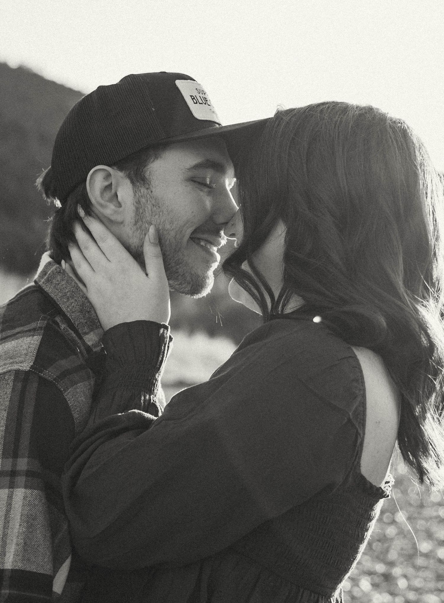 An intimate black and white portrait of a couple sharing a tender moment outdoors.