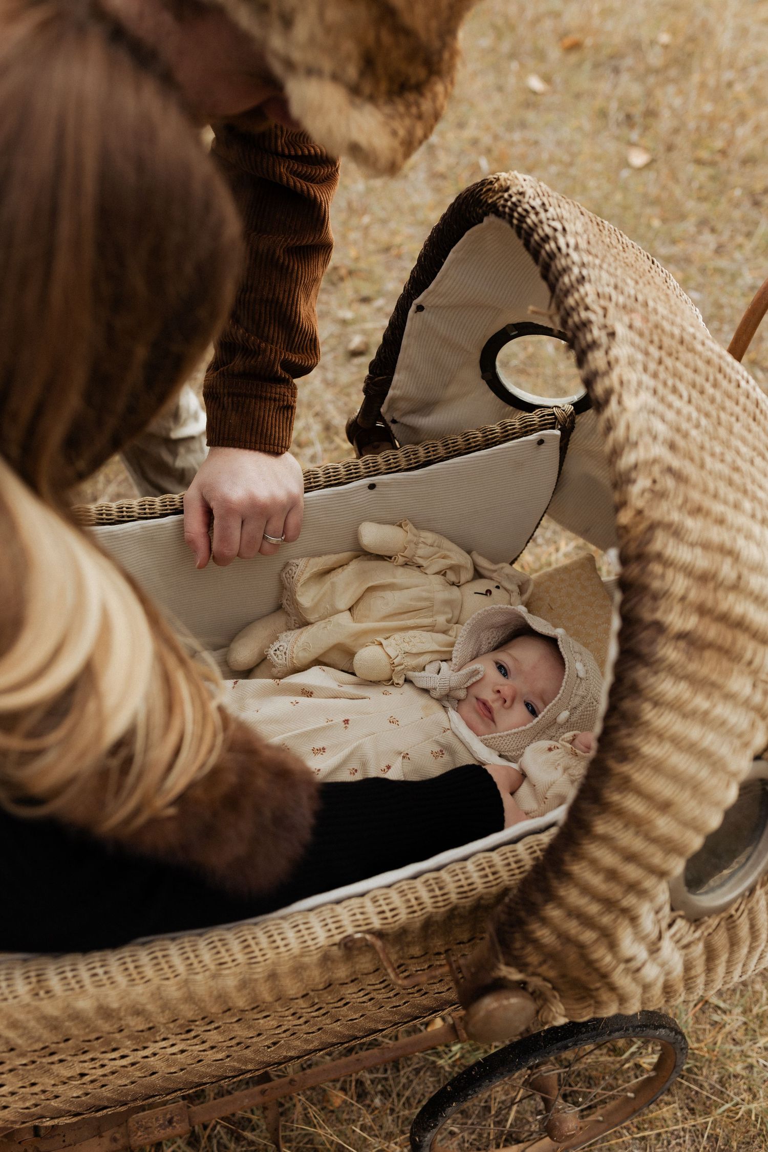Baby resting in vintage wicker carriage with parents looking on.