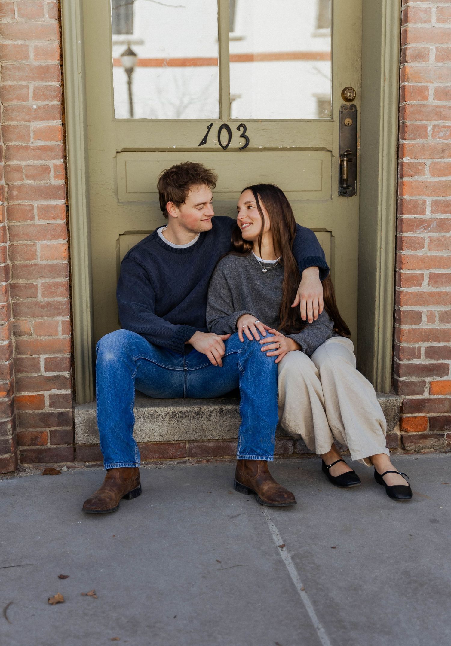 A couple sitting together on a doorstep marked 103 sharing a relaxed moment.