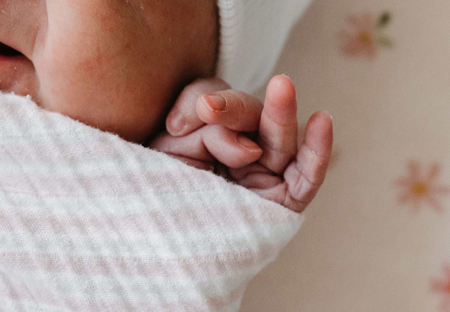Close-up view of a baby's tiny fingers gripping a white textured blanket against a floral background.