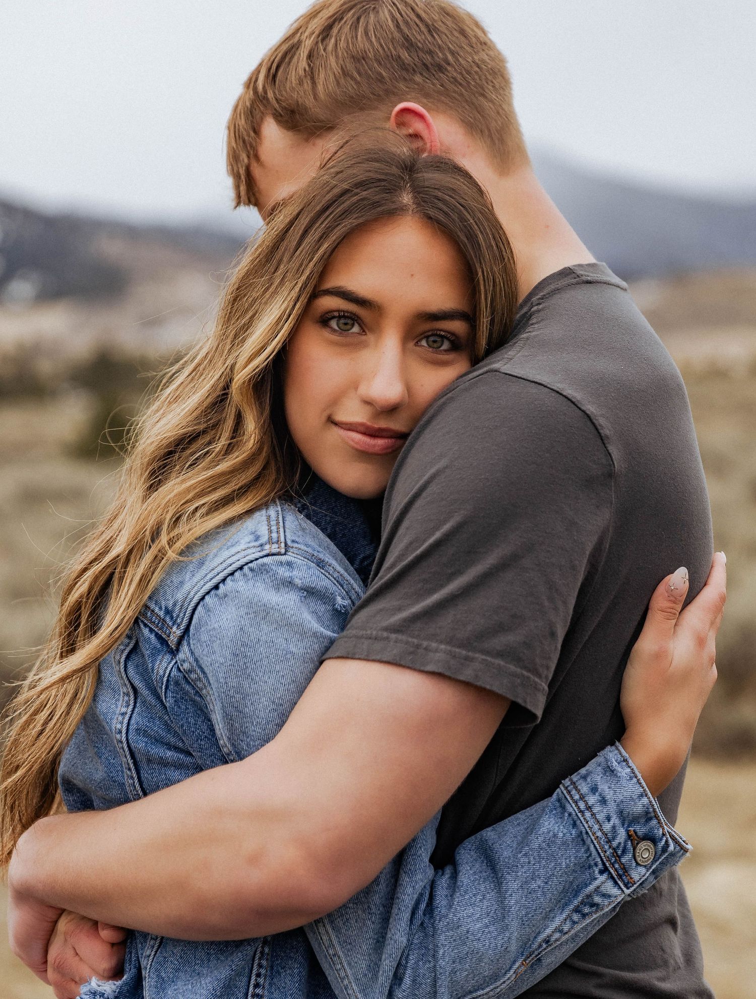 A tender embrace captured in a rustic mountain setting with soft natural lighting.