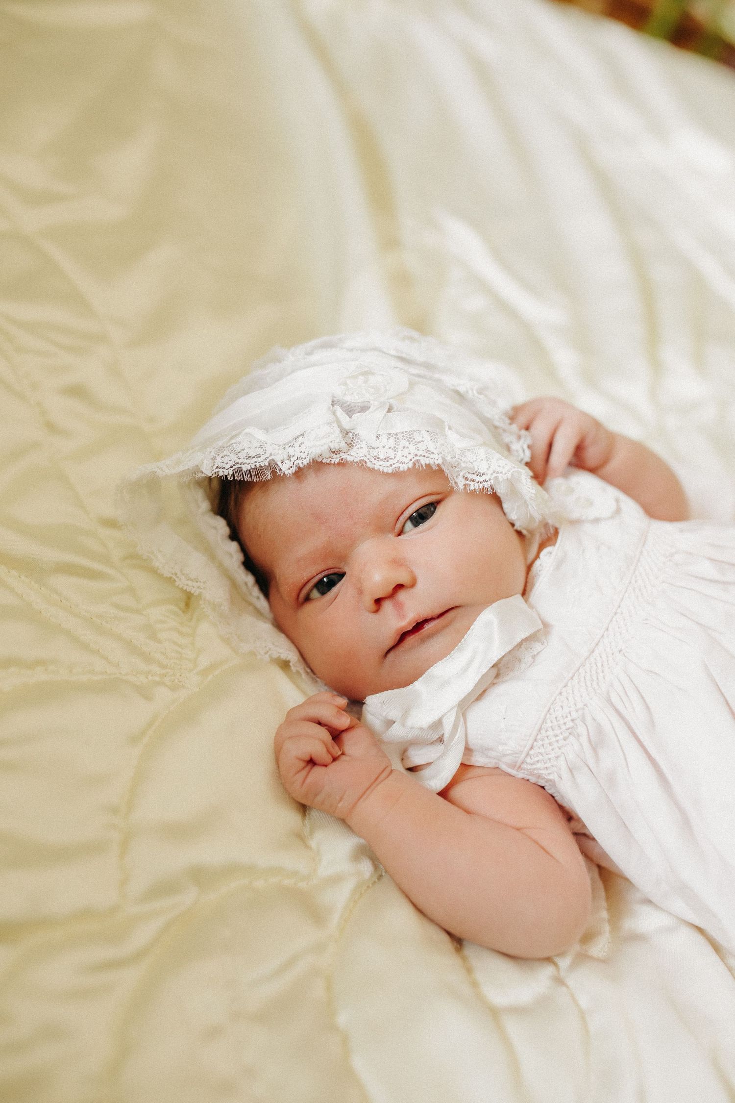 A newborn baby, laying on a visage blanket, stretches her arms.