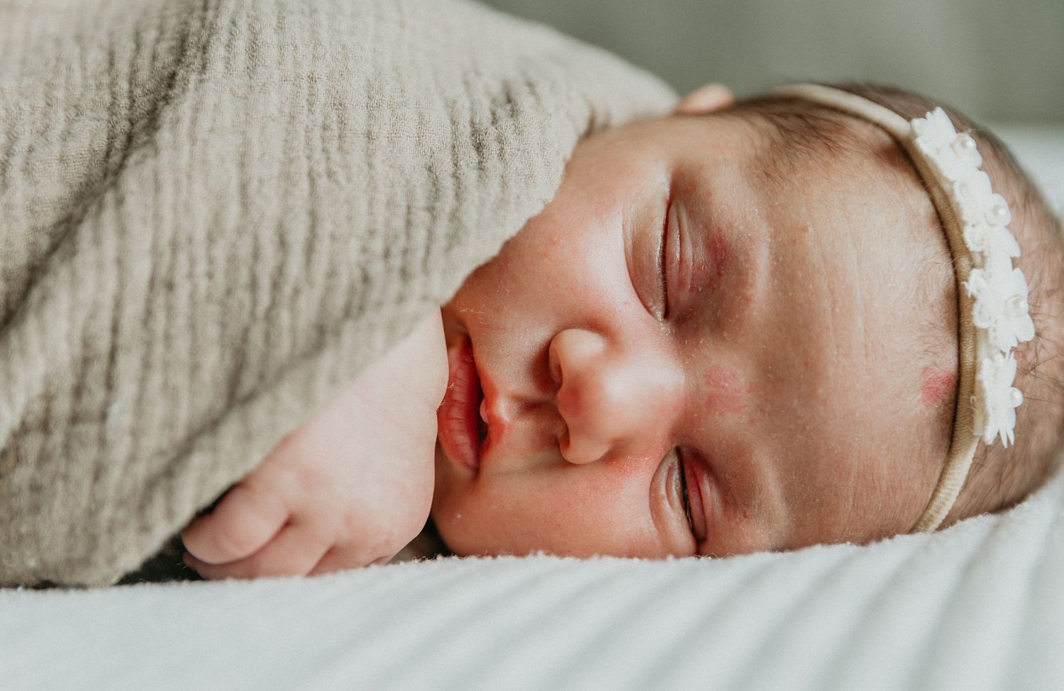 a sweet newborn baby swaddled on a cozy best in natural light during her in home session
