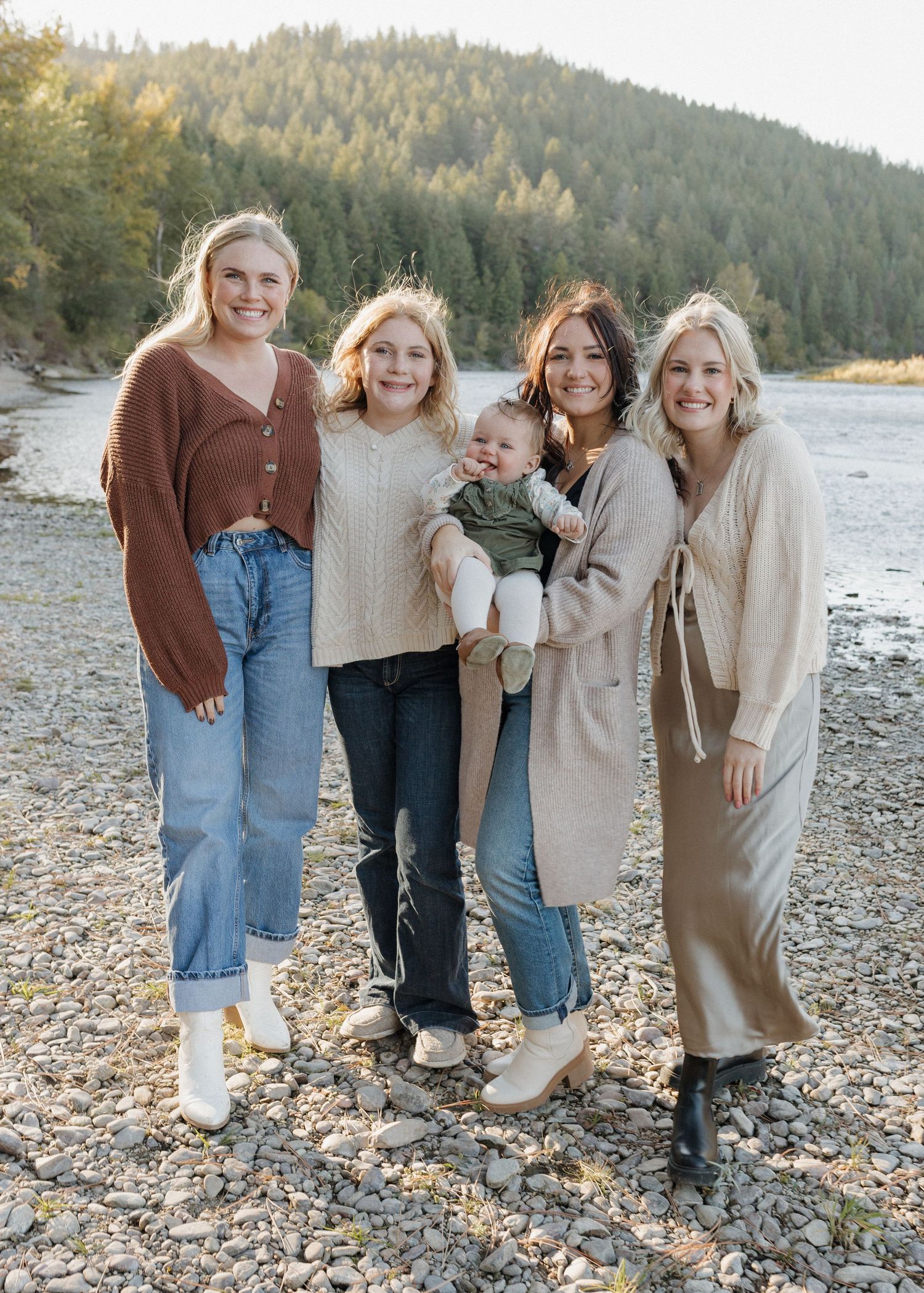 Group portrait of women and baby standing together on rocky shoreline with mountain views.