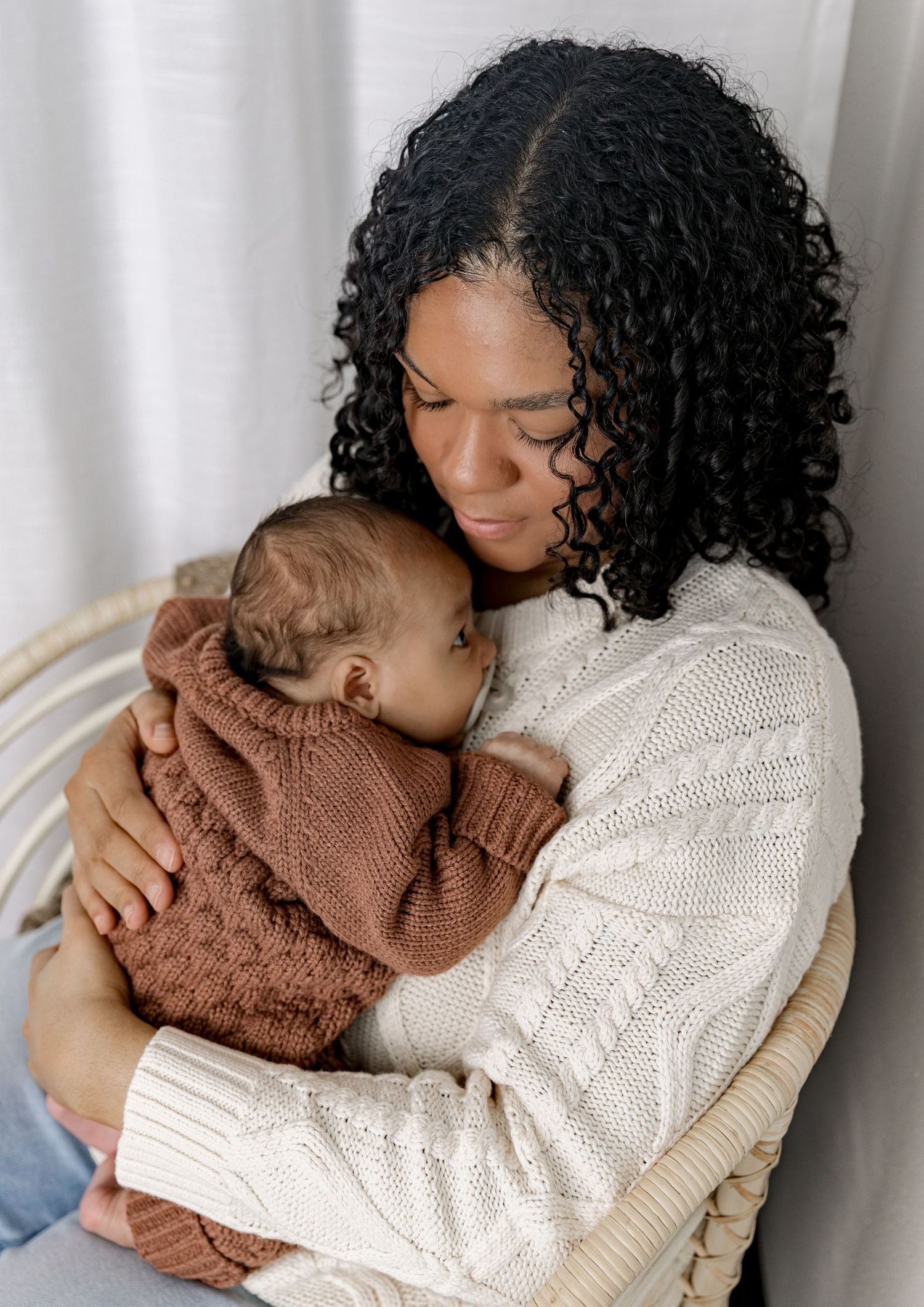Two people in cozy knit sweaters embrace tenderly against a white curtain background in a series of intimate photos.
