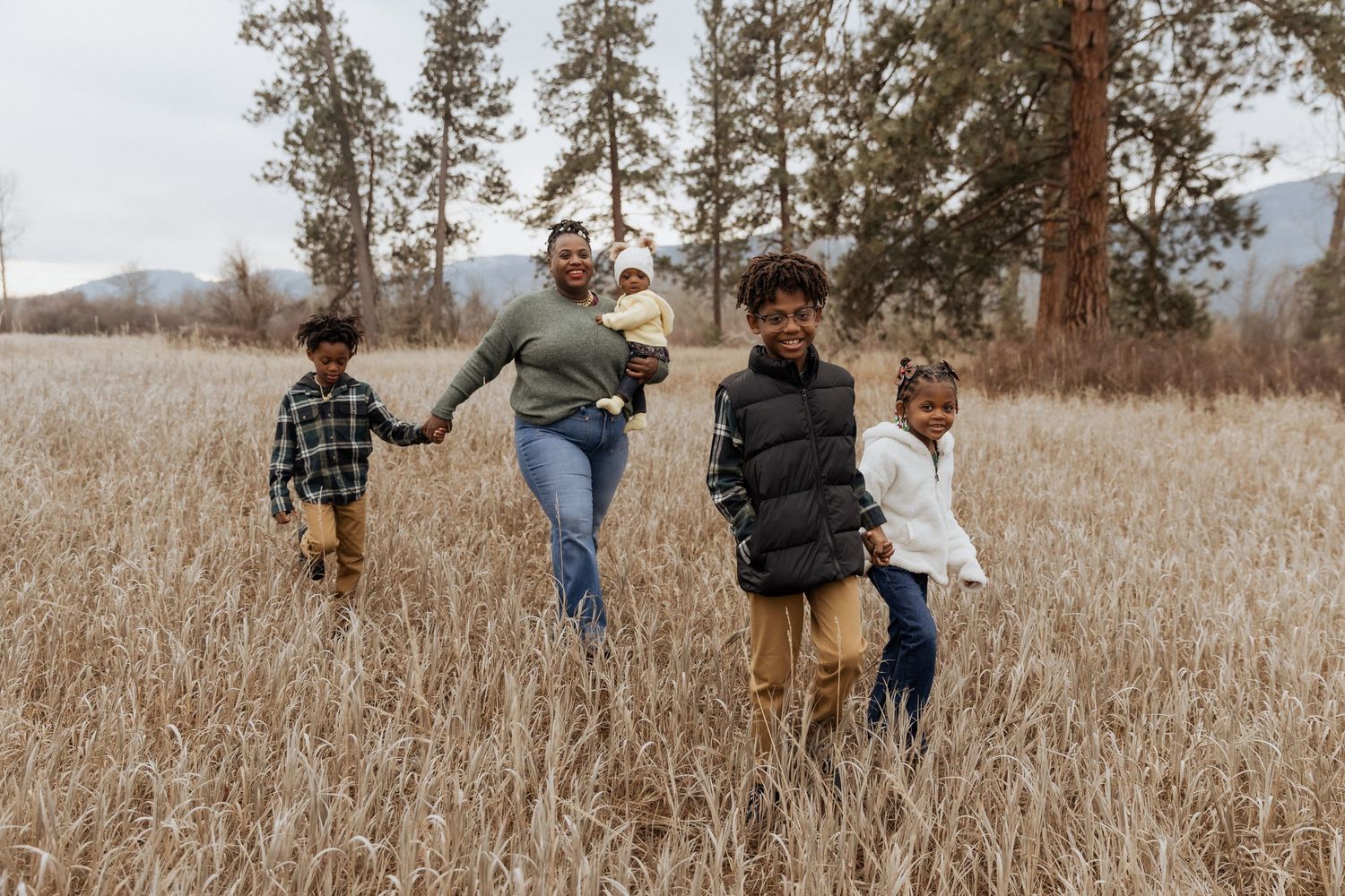 Family walking through tall grass field with mountains and trees in background.