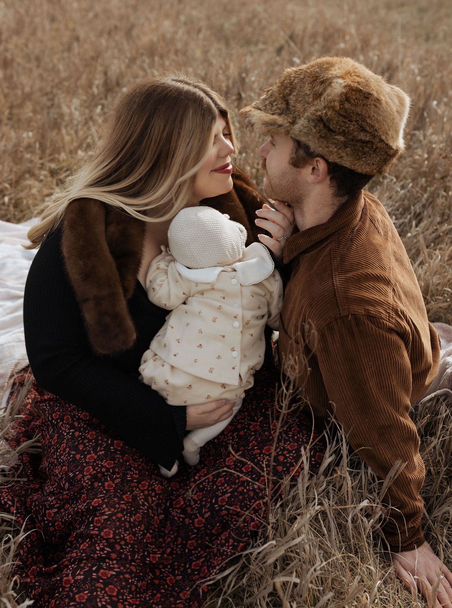 Intimate family moment with baby in white outfit against autumn landscape.