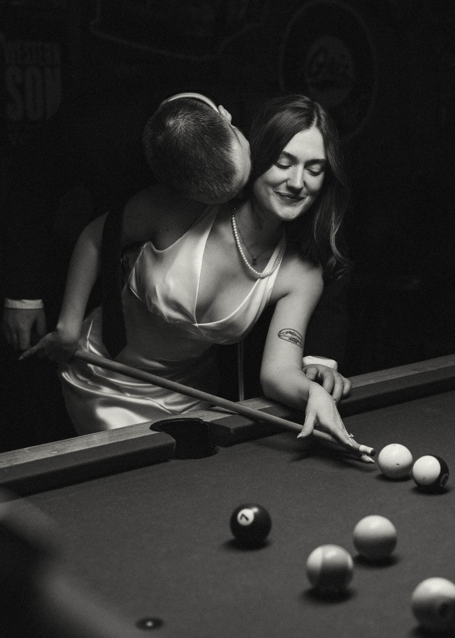 Couple playing pool in a dimly lit bar with black and white aesthetic.