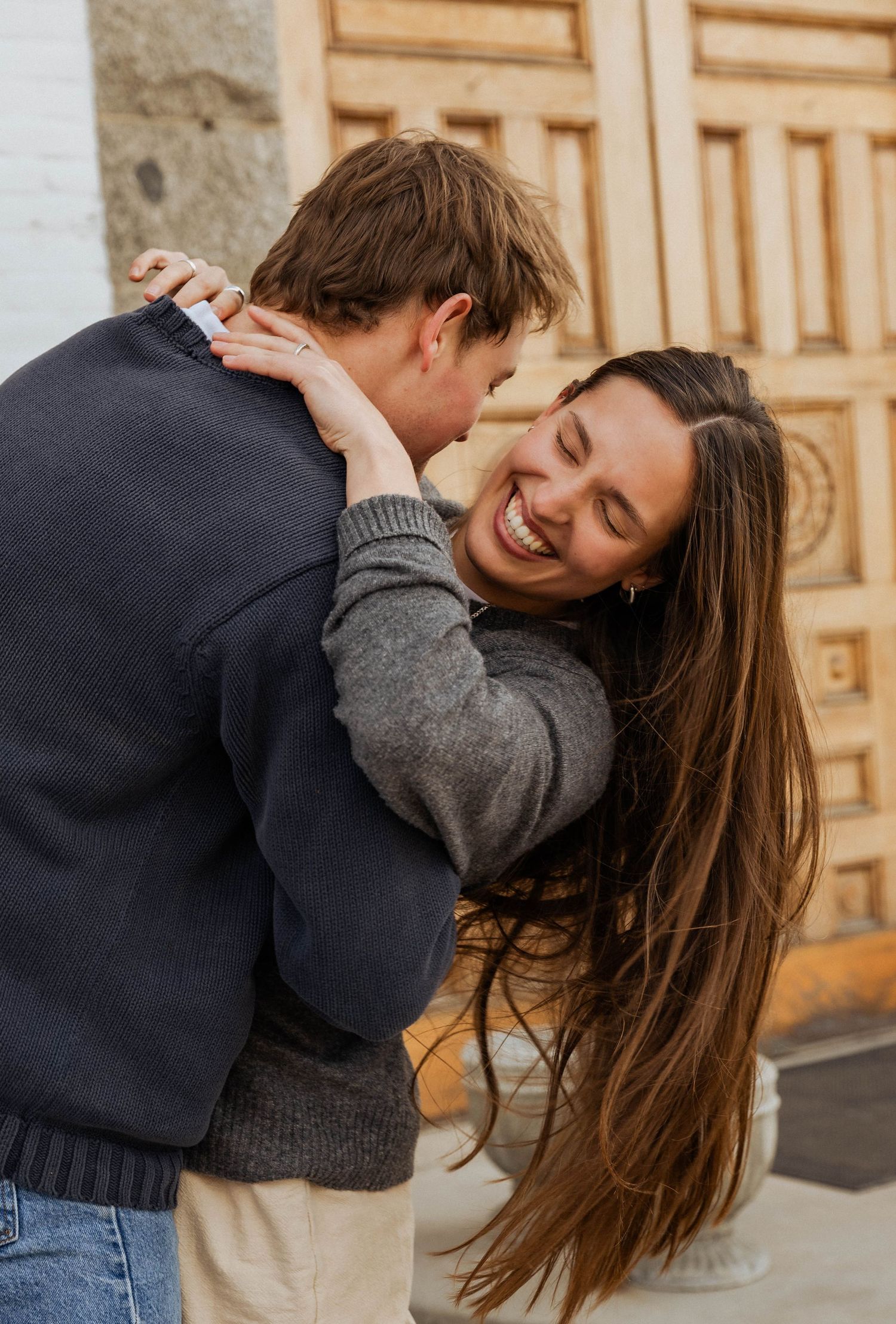 A playful moment between a couple laughing and embracing against wooden doors.