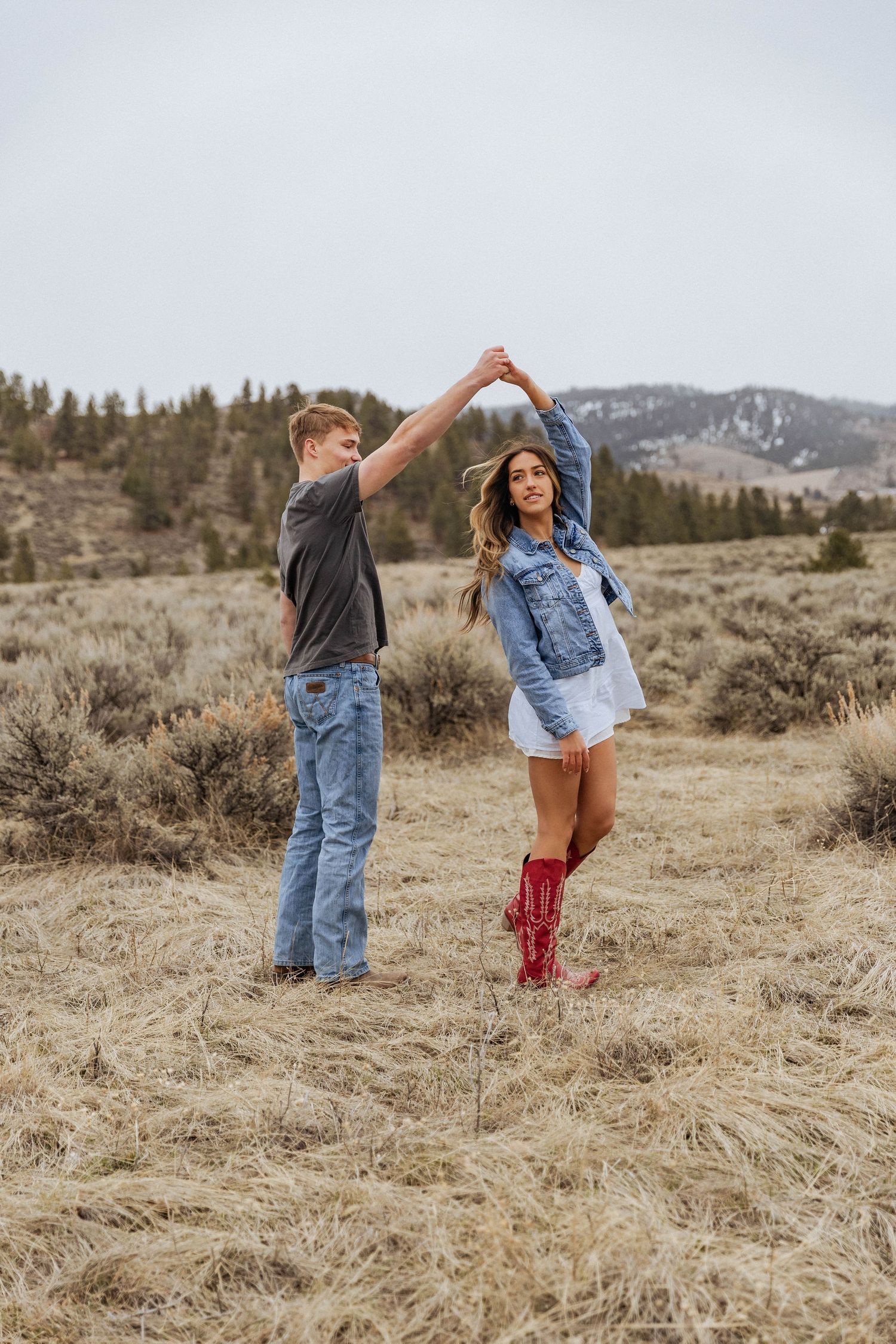 Dancing outdoors in a mountain meadow wearing casual denim and red boots.