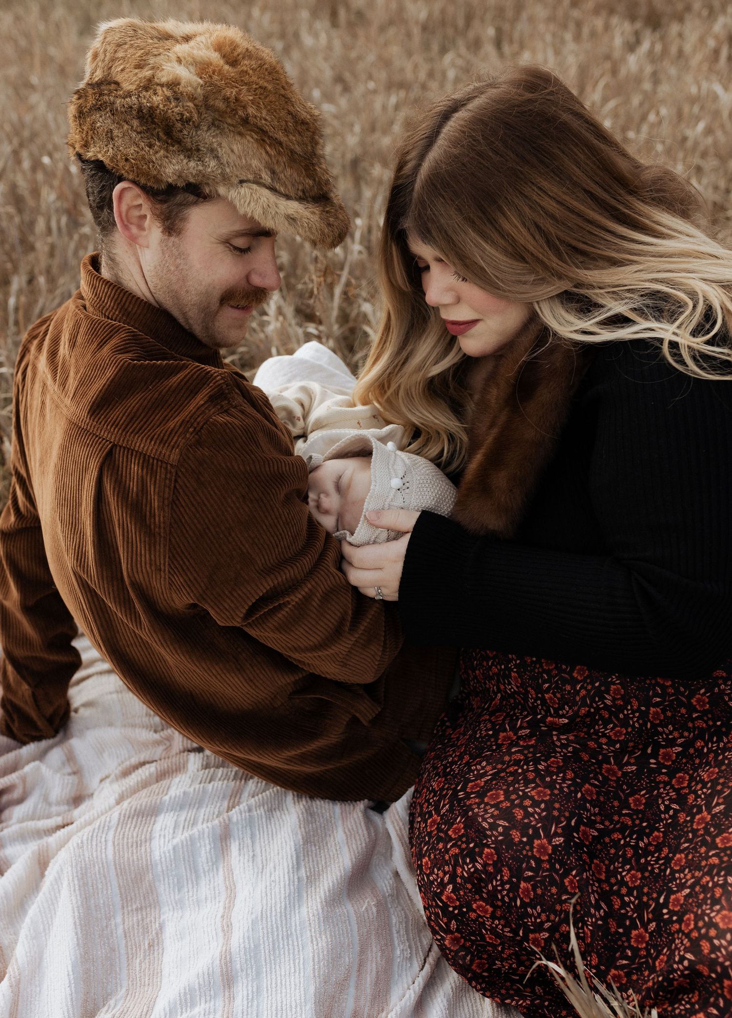 Intimate family moment with parents cradling infant in golden autumn field.