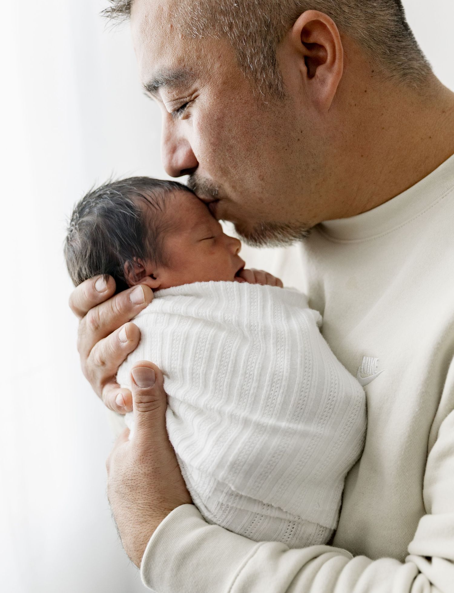 A tender moment between a parent in a cream sweater and a small baby wrapped in a white blanket.