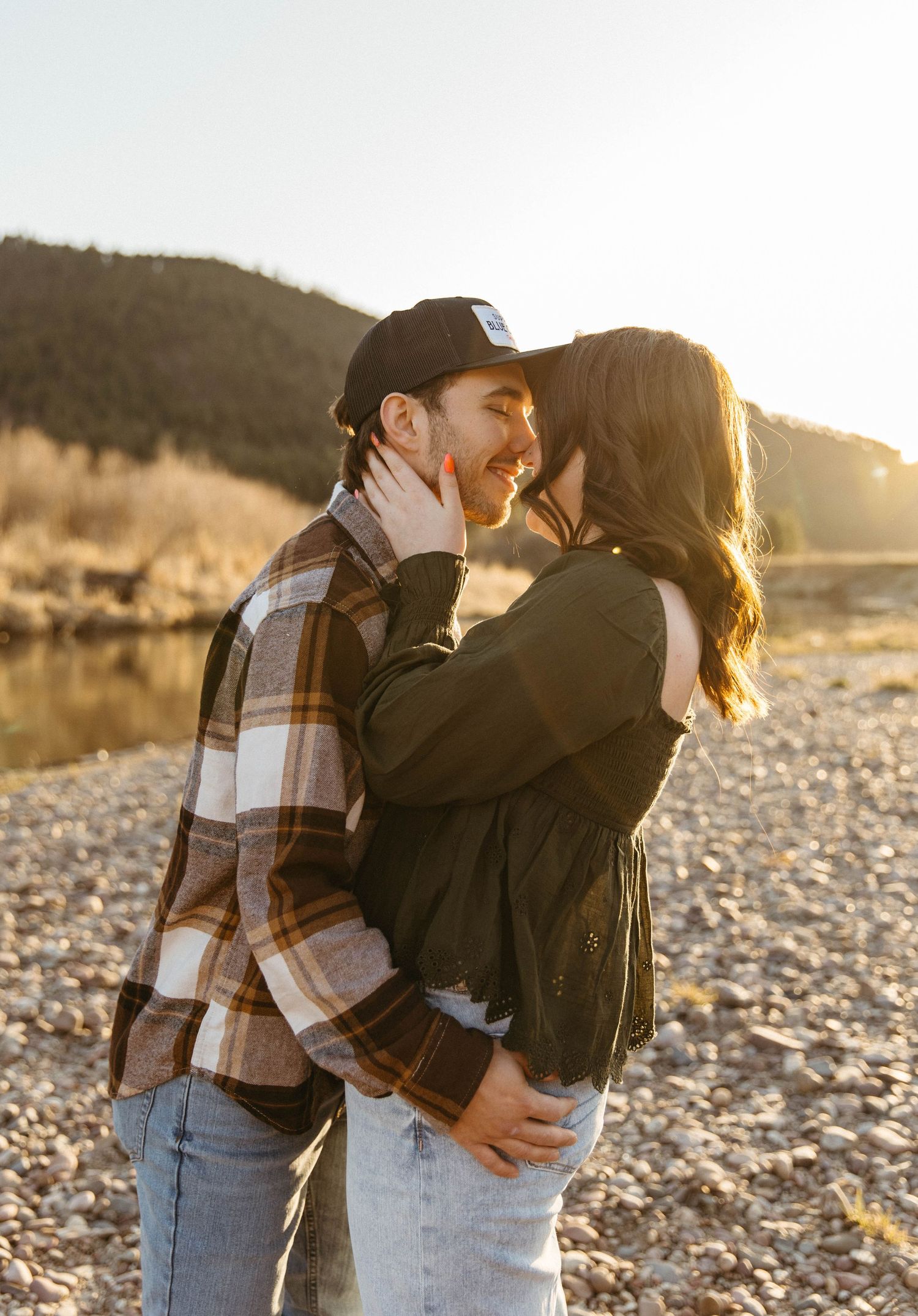 A couple sharing an intimate moment by a lake during sunset.