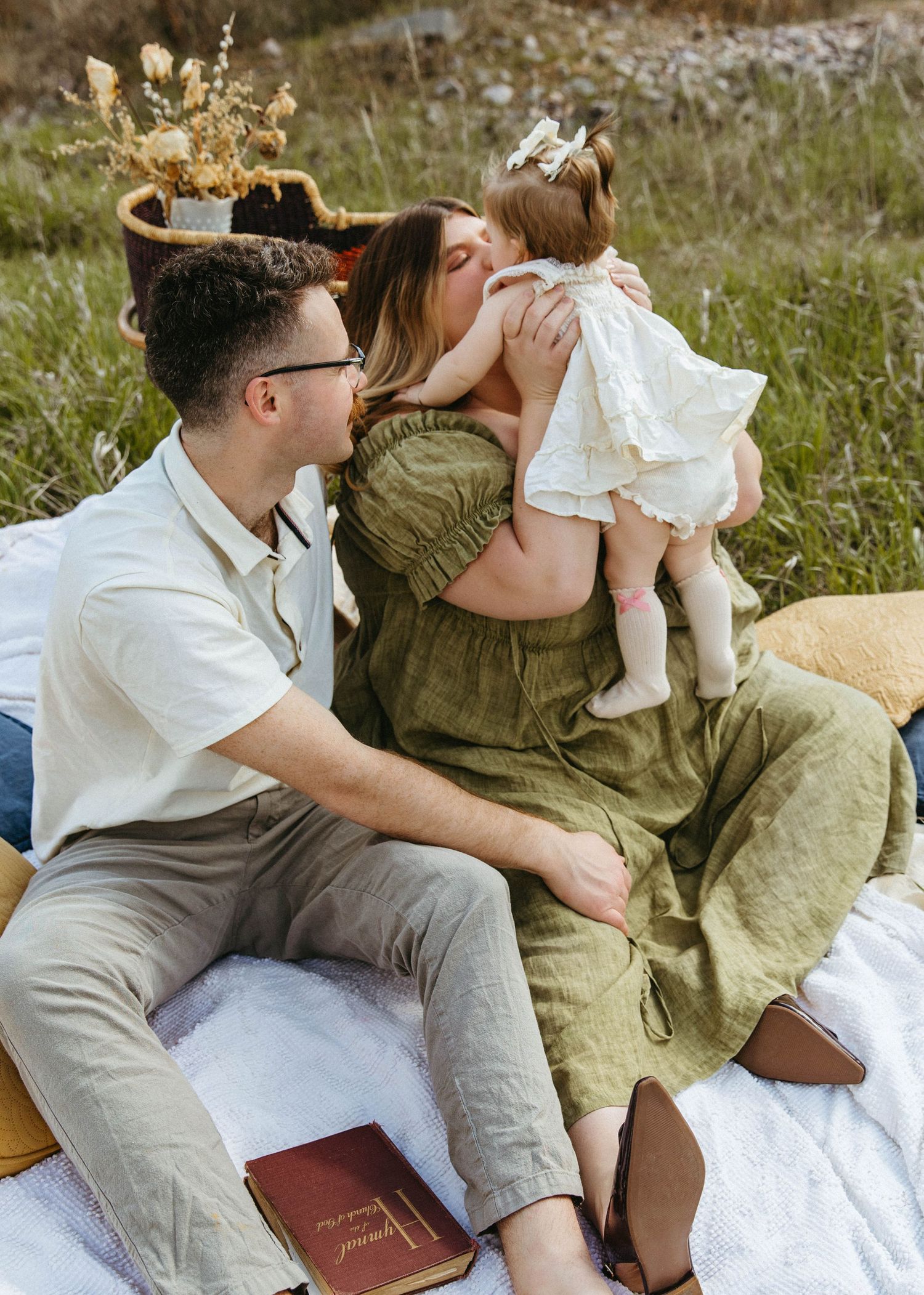 A couple shares a tender romantic moment on a picnic blanket outdoors with a book nearby.