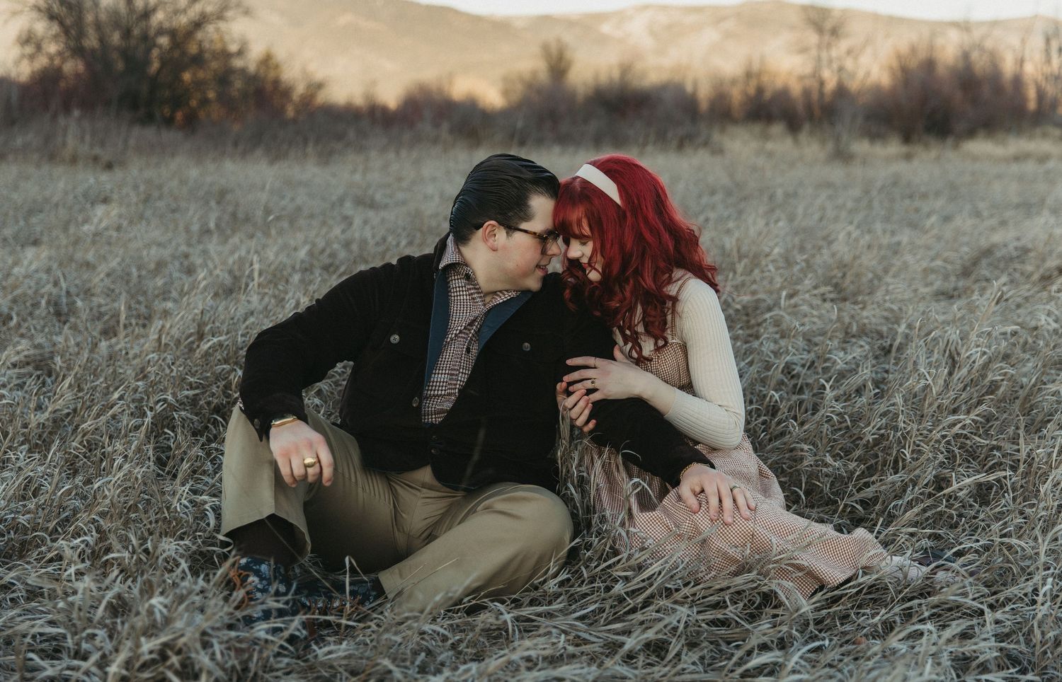 Romantic couple shares intimate moments in a rustic field during golden hour sunset.