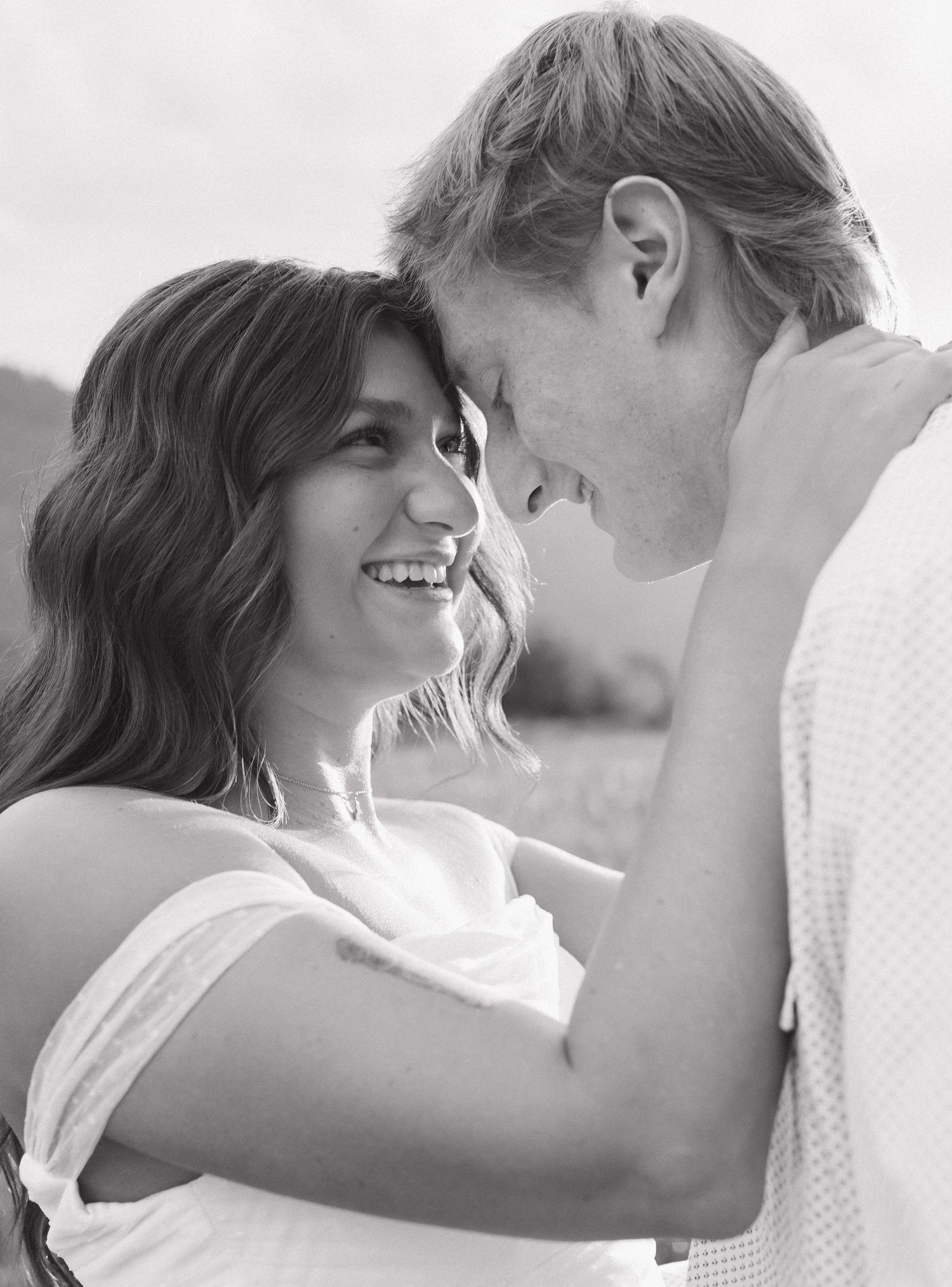 Black and white portrait of couple in tender embrace against nature backdrop.