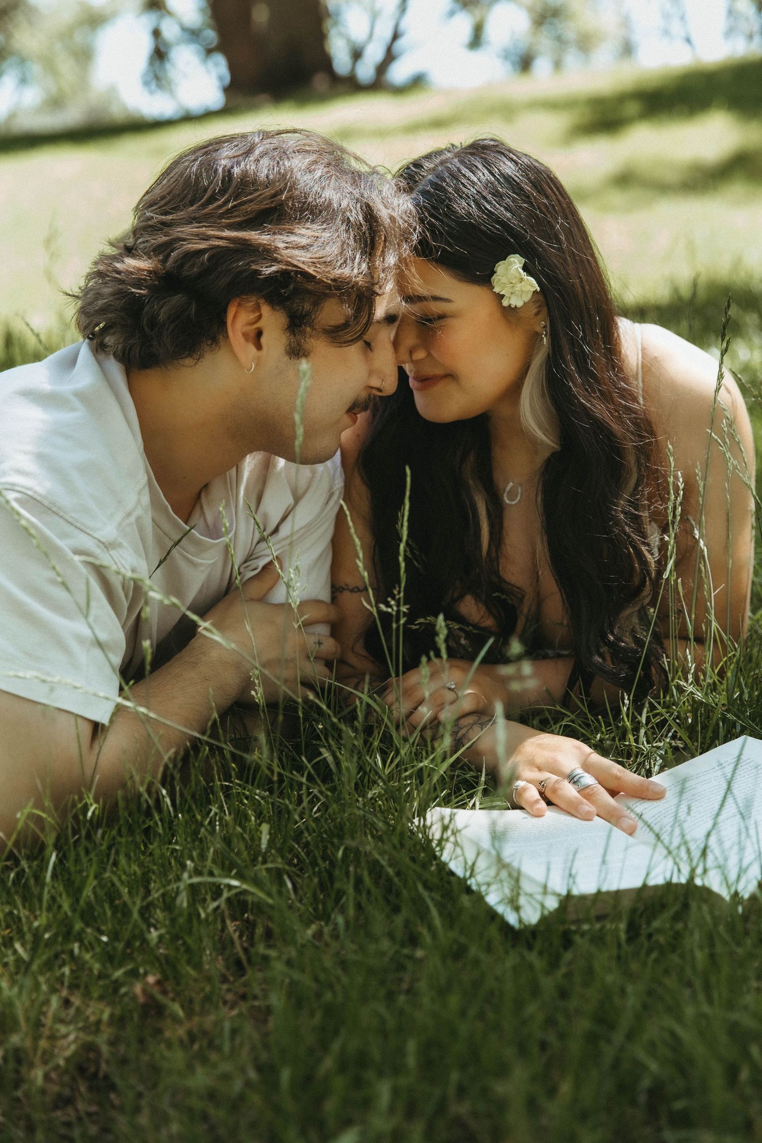 A romantic couple lies in green grass together sharing an intimate moment on a sunny day.