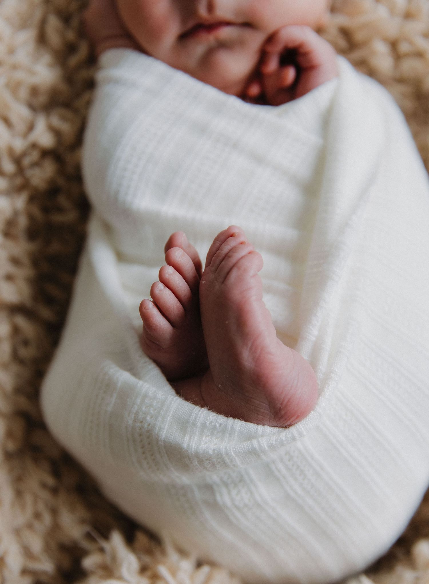 Close-up of tiny baby feet peeking out from white swaddle blanket.