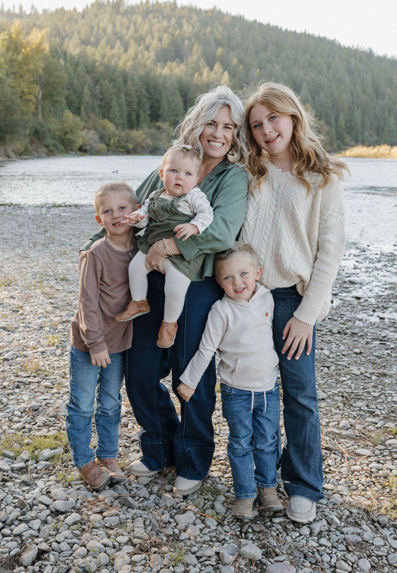 Family of five posed together on rocky riverbank with forested hillside in background.