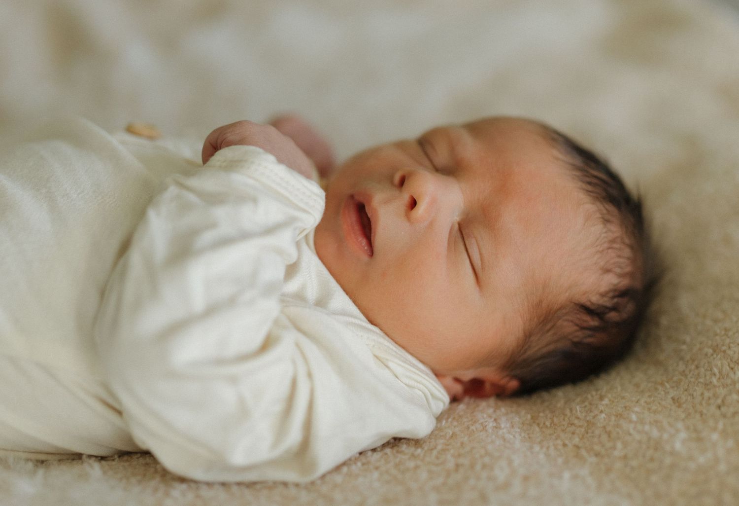 Sleeping infant in white sleeper resting on beige textured blanket.