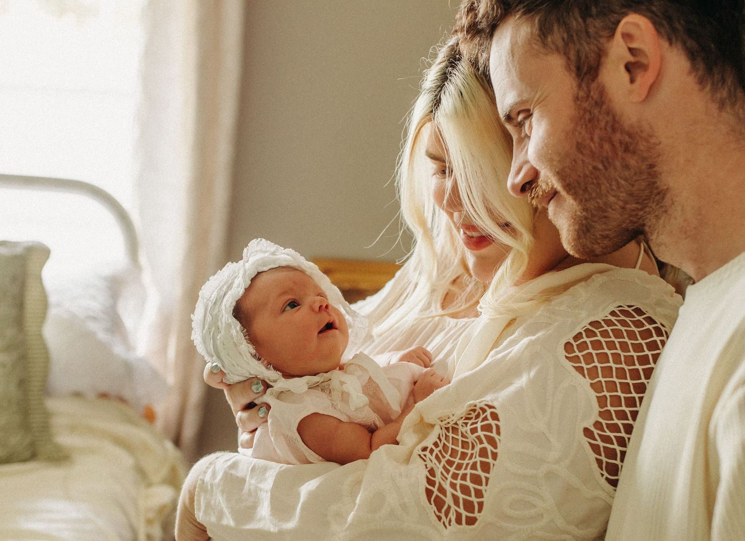 A sweet family moment with parents admiring their newborn baby dressed in white lace.