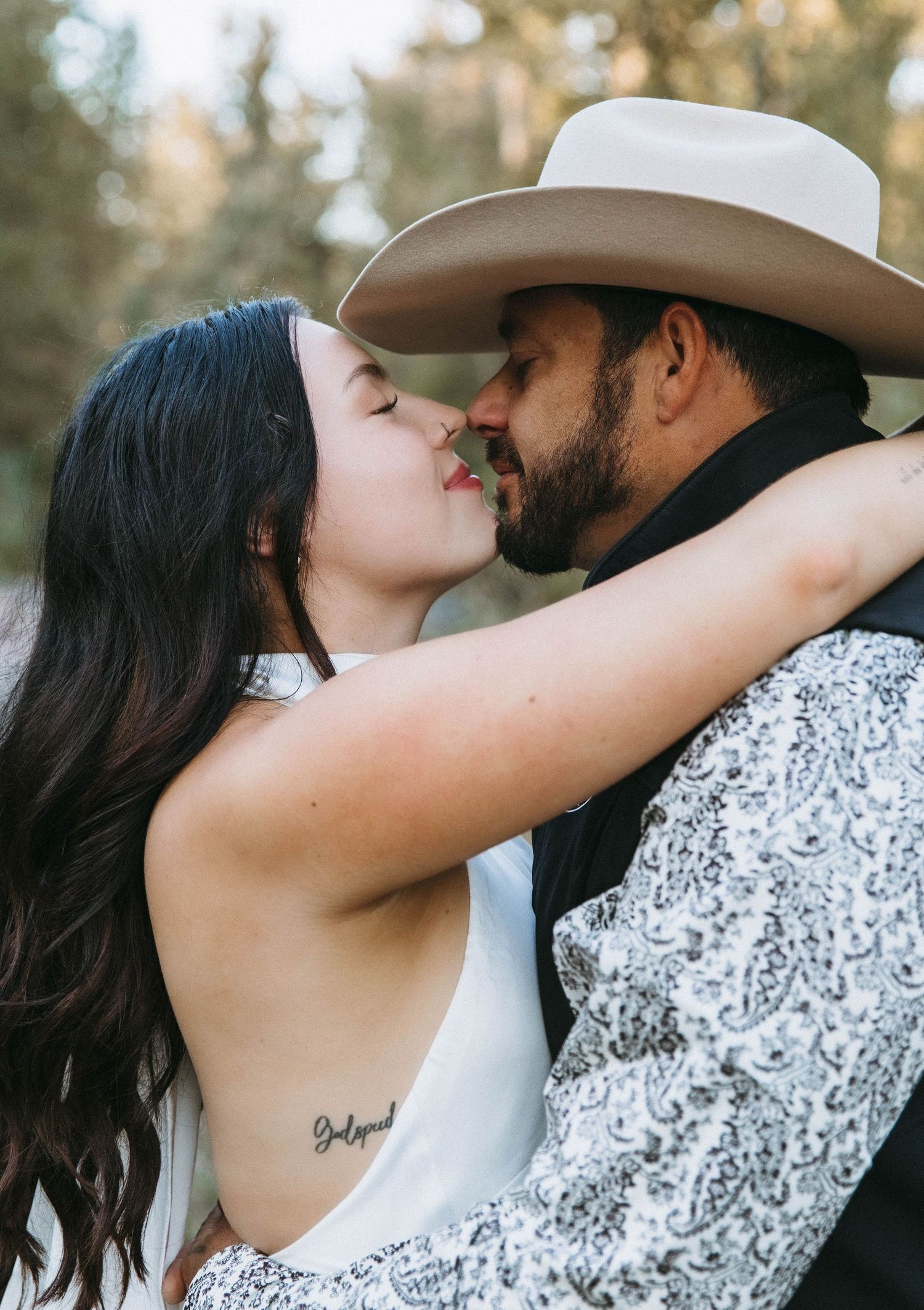 A romantic couple sharing tender kisses while wearing western attire against a soft outdoor background.