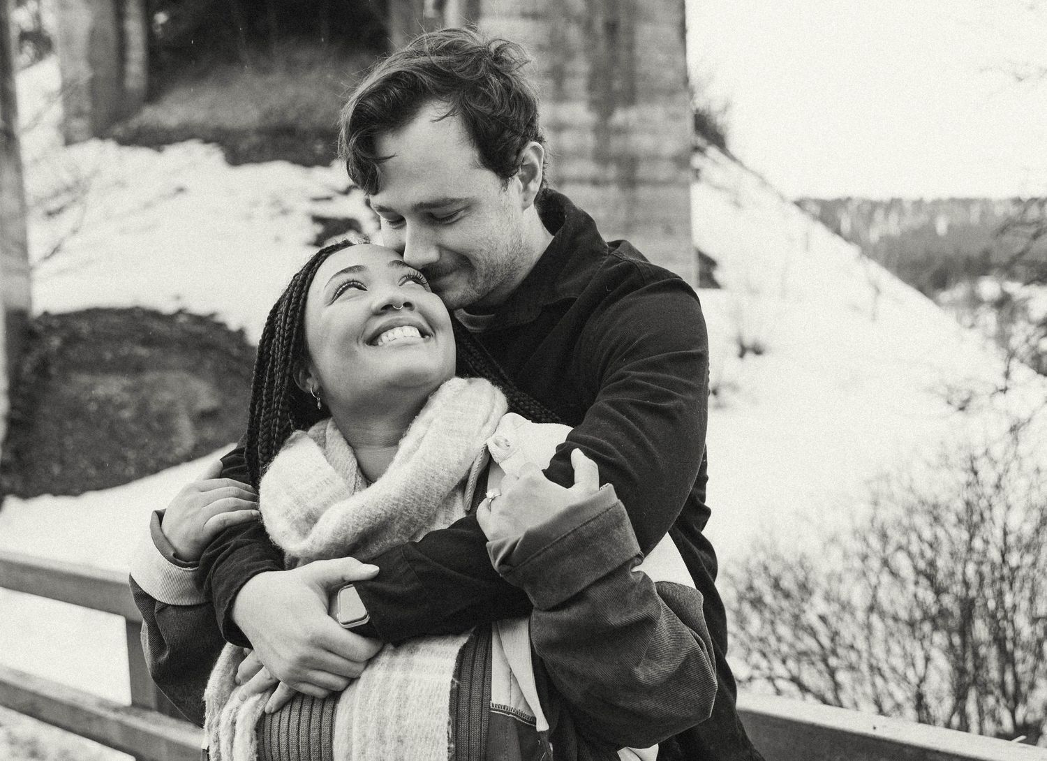 A romantic black and white photograph capturing an intimate winter embrace outdoors.