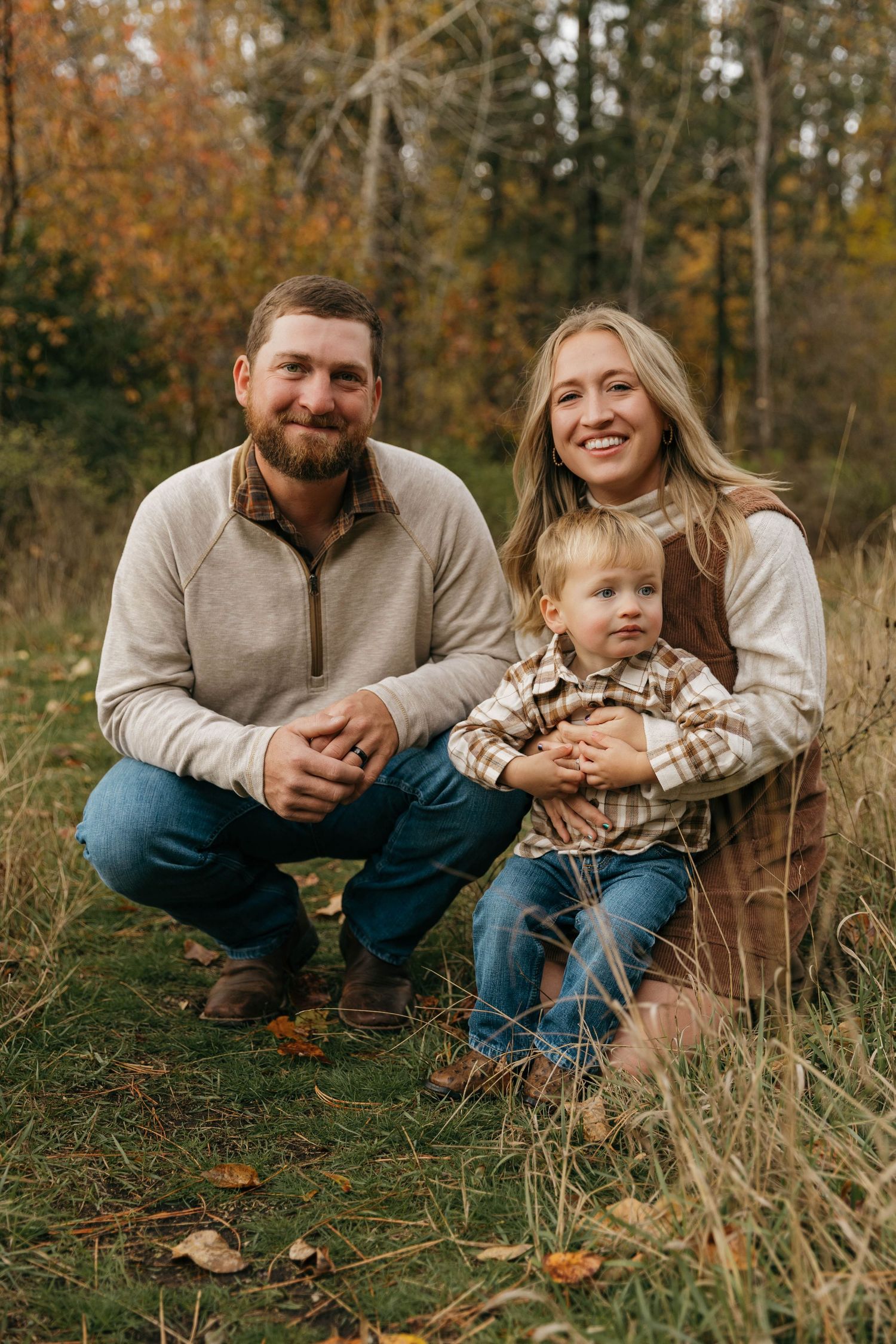 A family sits together in autumn grass surrounded by fallen leaves during an outdoor photo session.