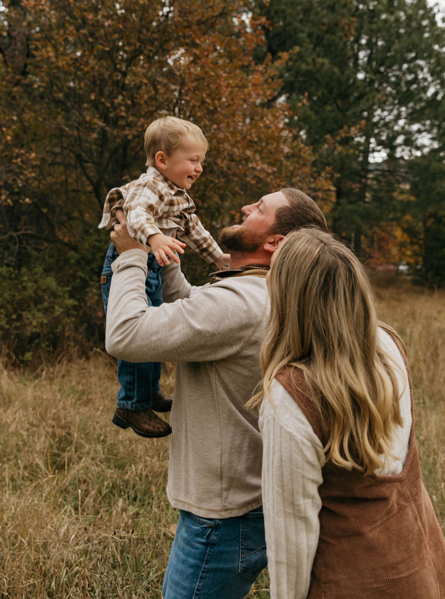 A family shares a joyful autumn moment together in a field with fall foliage in the background.