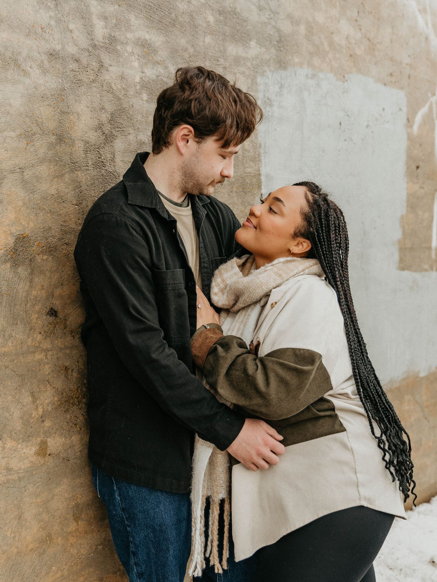 Couple embracing against textured wall during winter photoshoot.