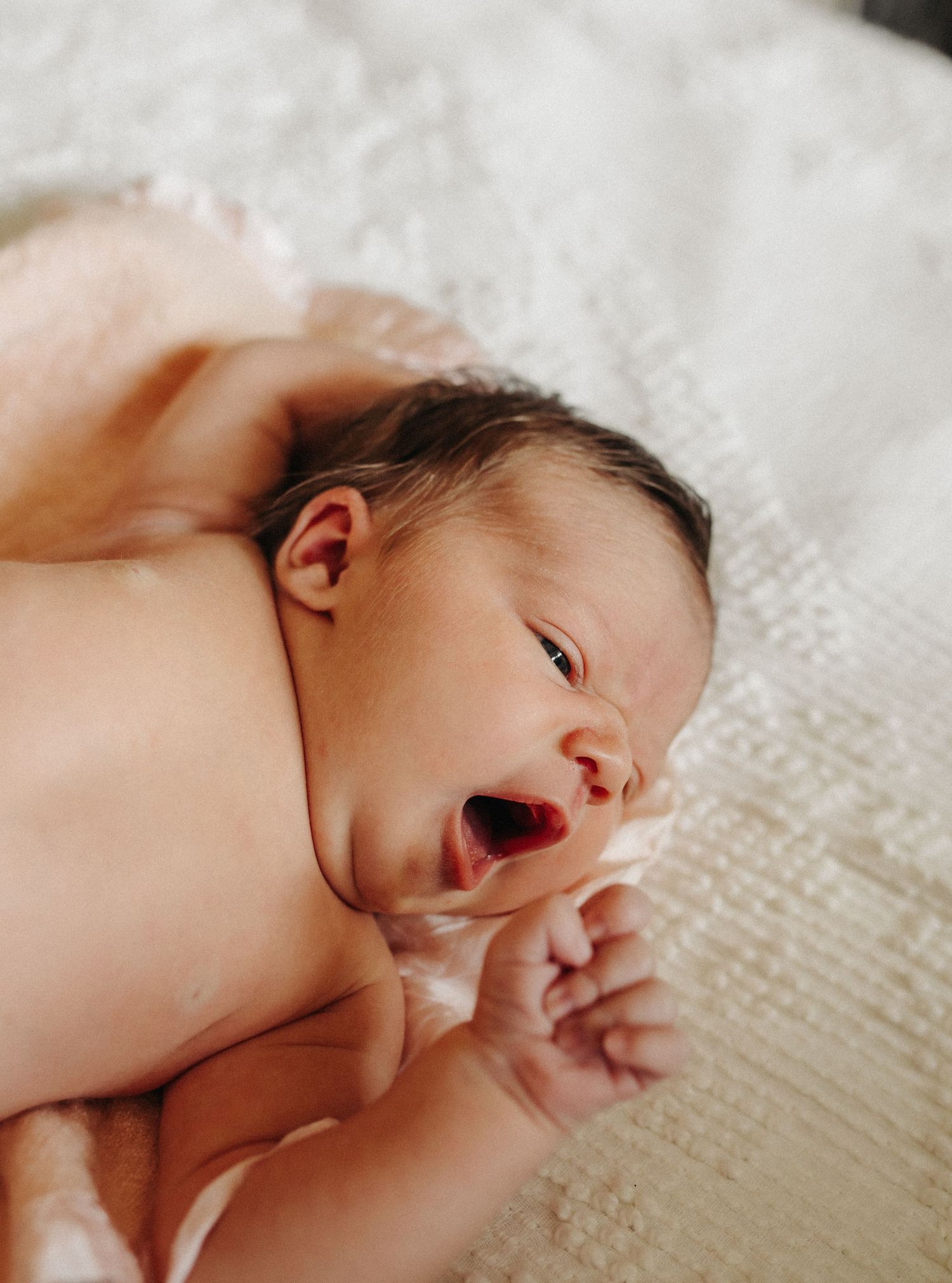 A newborn baby, laying on a visage blanket, stretches her arms.