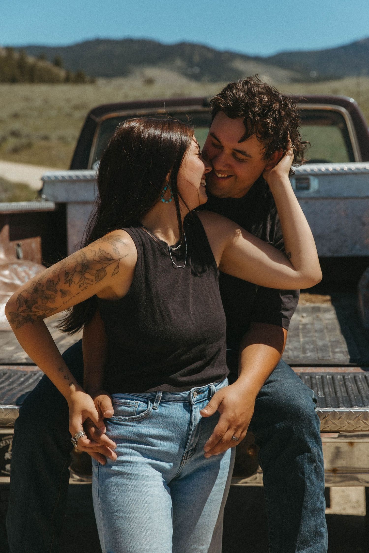 A couple shares romantic moments while sitting on a rustic wooden fence in a mountainous desert landscape.
