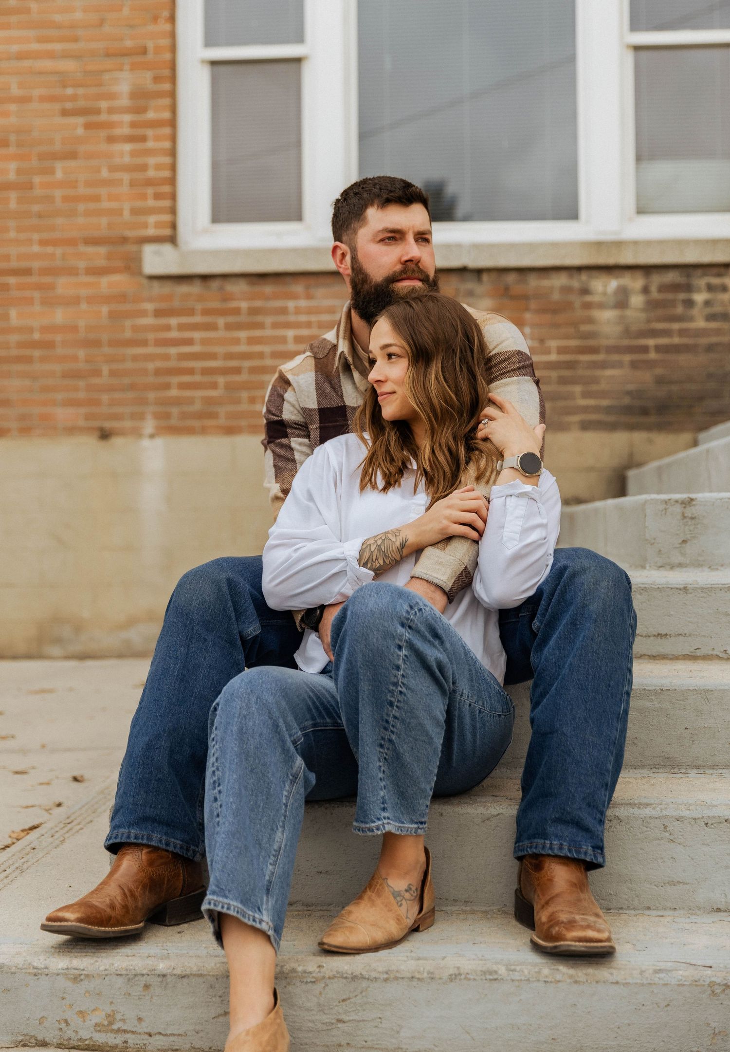 A couple in casual attire sitting together on concrete steps outside a brick building.