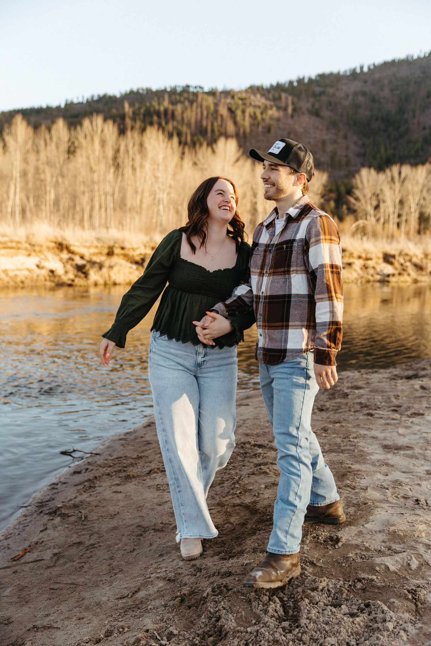 A romantic couple walking together along a lakeside trail during golden hour.