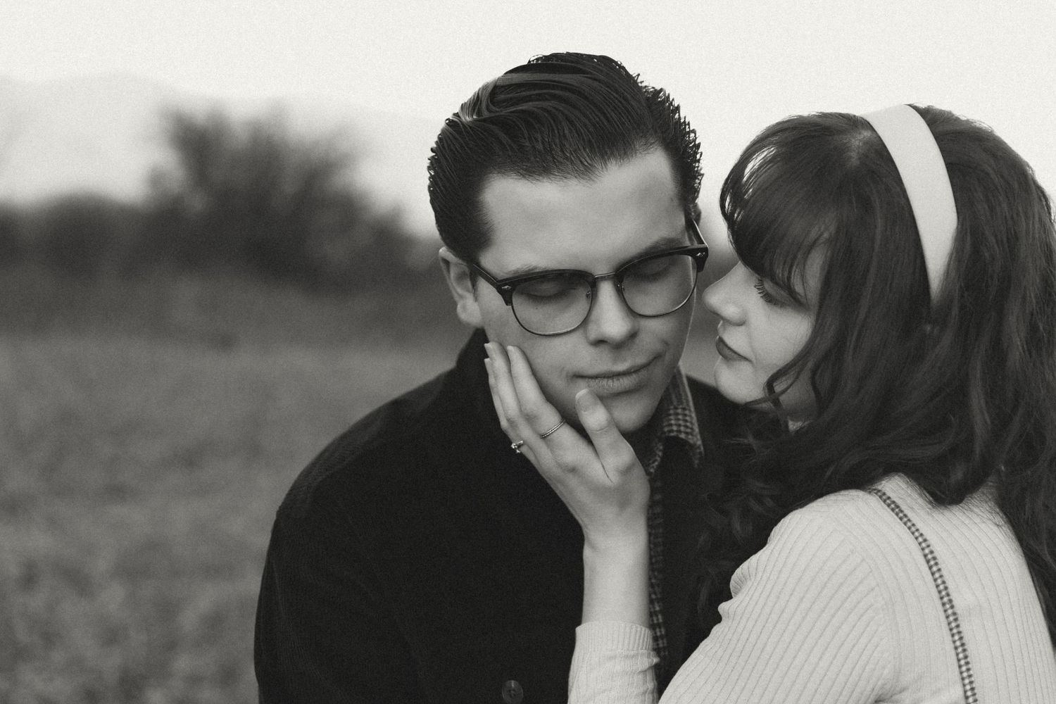 A romantic black and white photograph of a couple in the 1960s, with one person wearing glasses and a sweater.