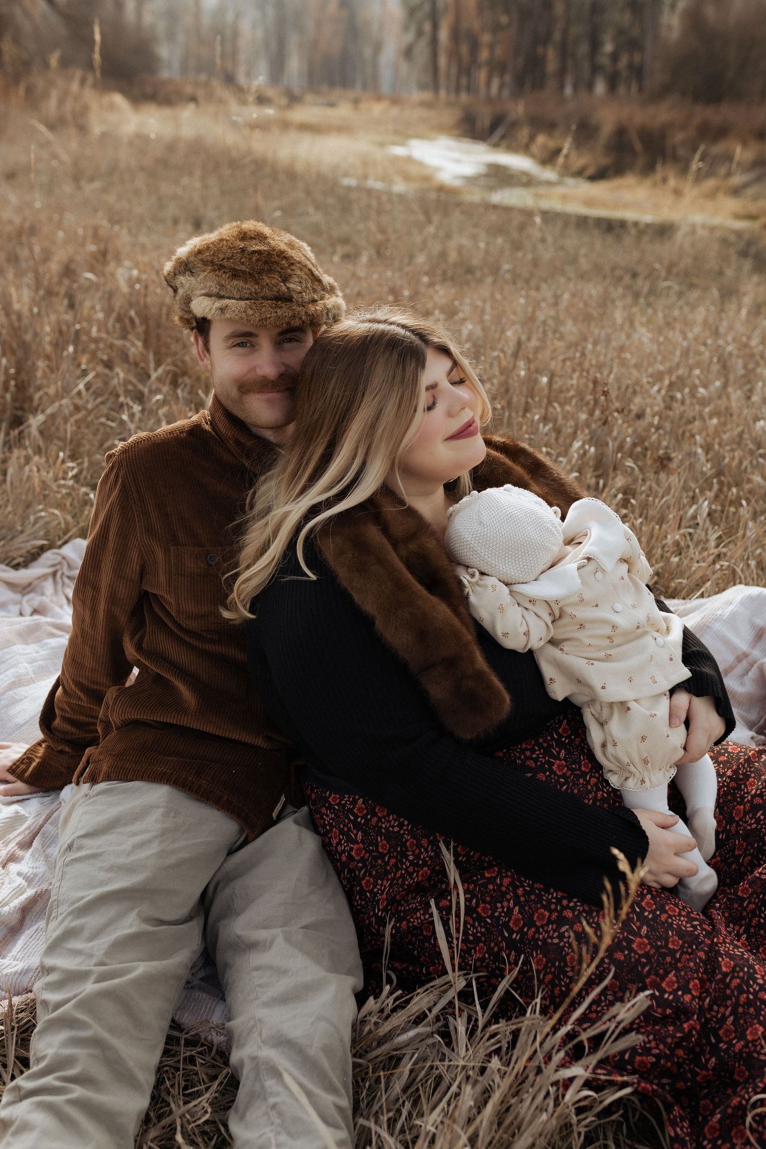 Family relaxing together on blanket in rustic autumn field setting.