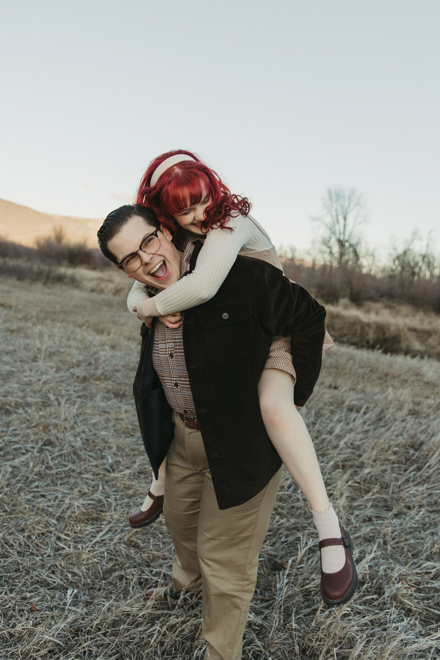 A playful couple embraces and laughs together in a field during golden hour.