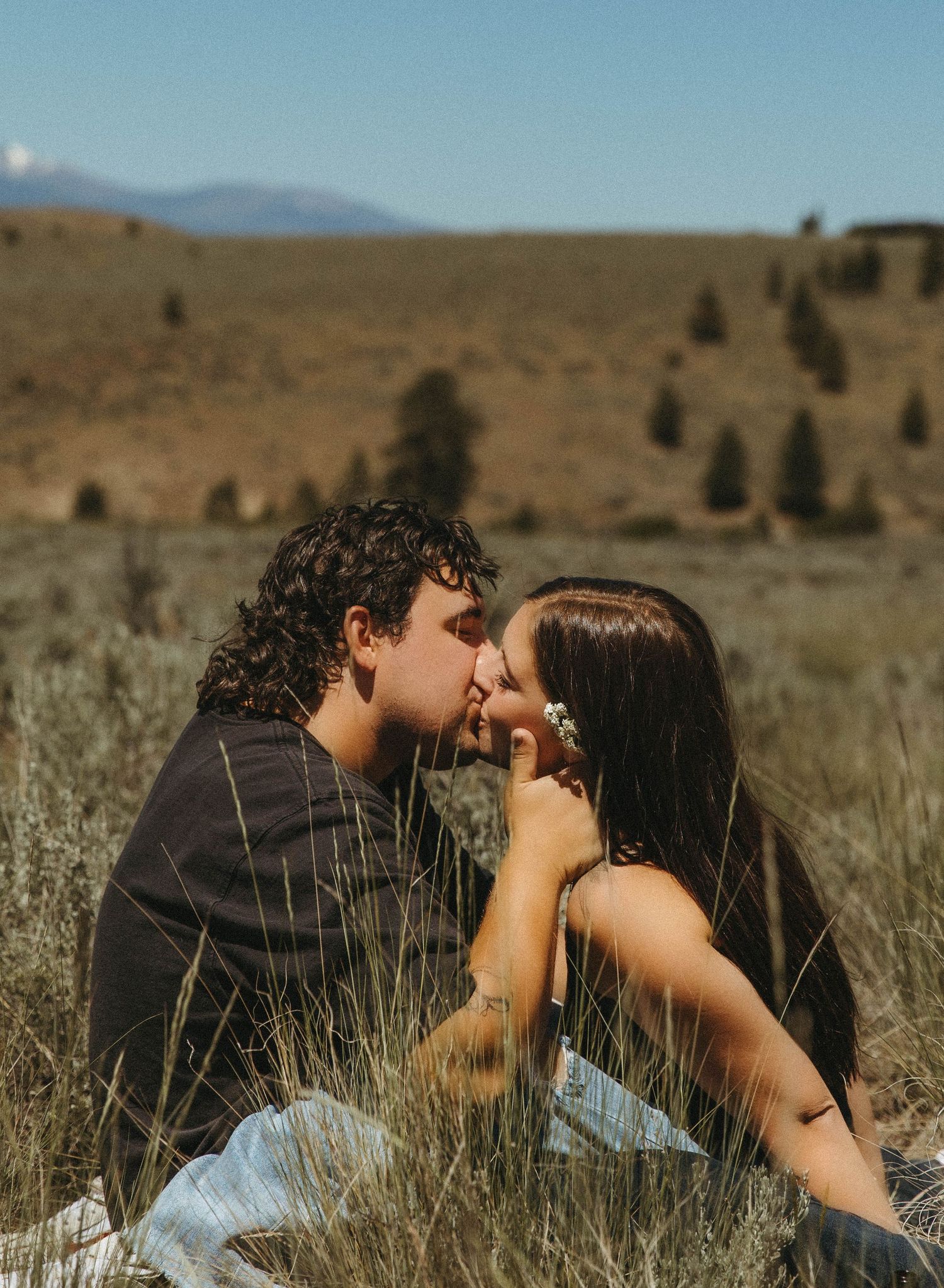 A couple embraces intimately amidst wild grasses with a mountainous desert landscape behind them.