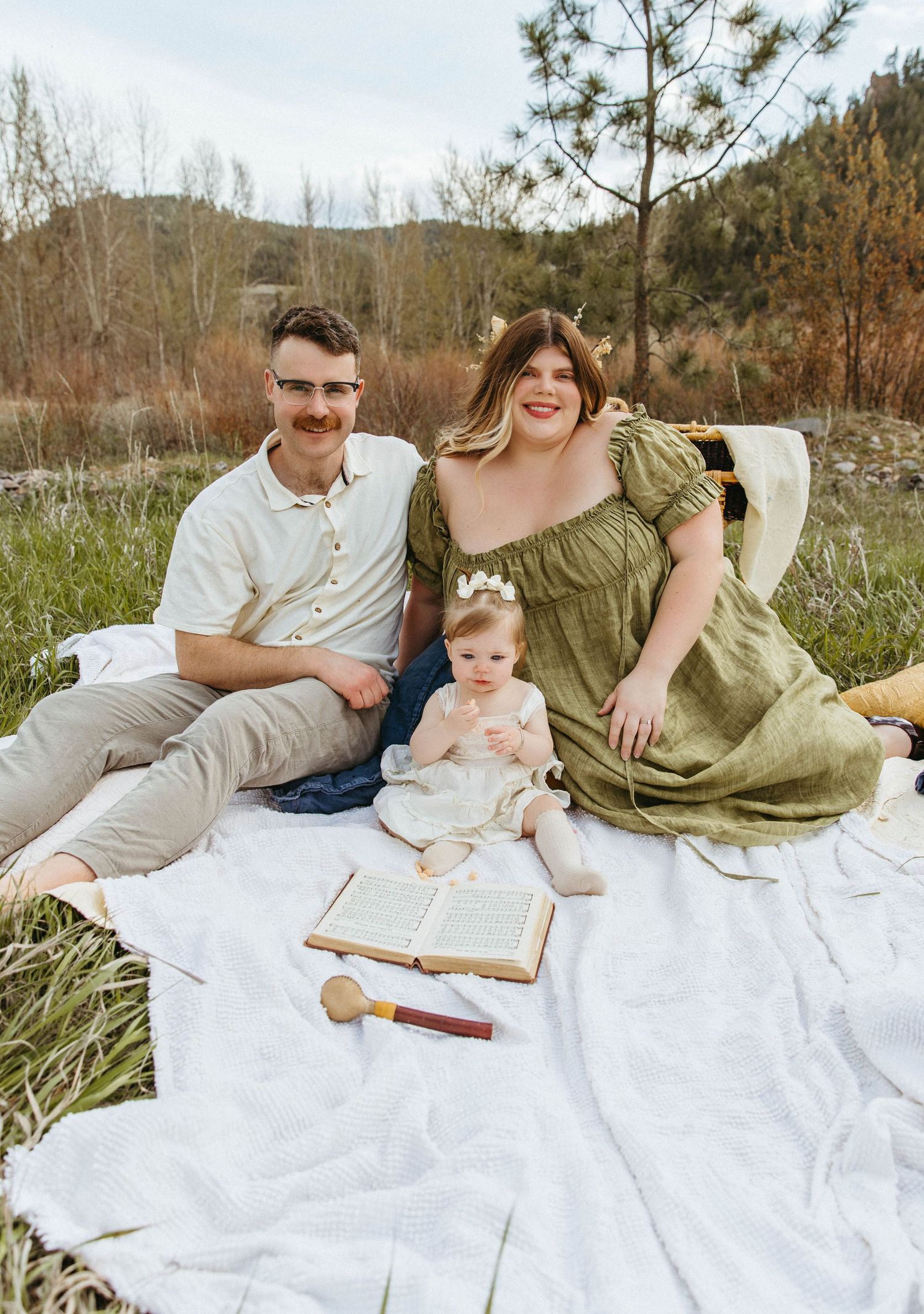 Outdoor family picnic scene with white blanket and vintage book on grassy field.