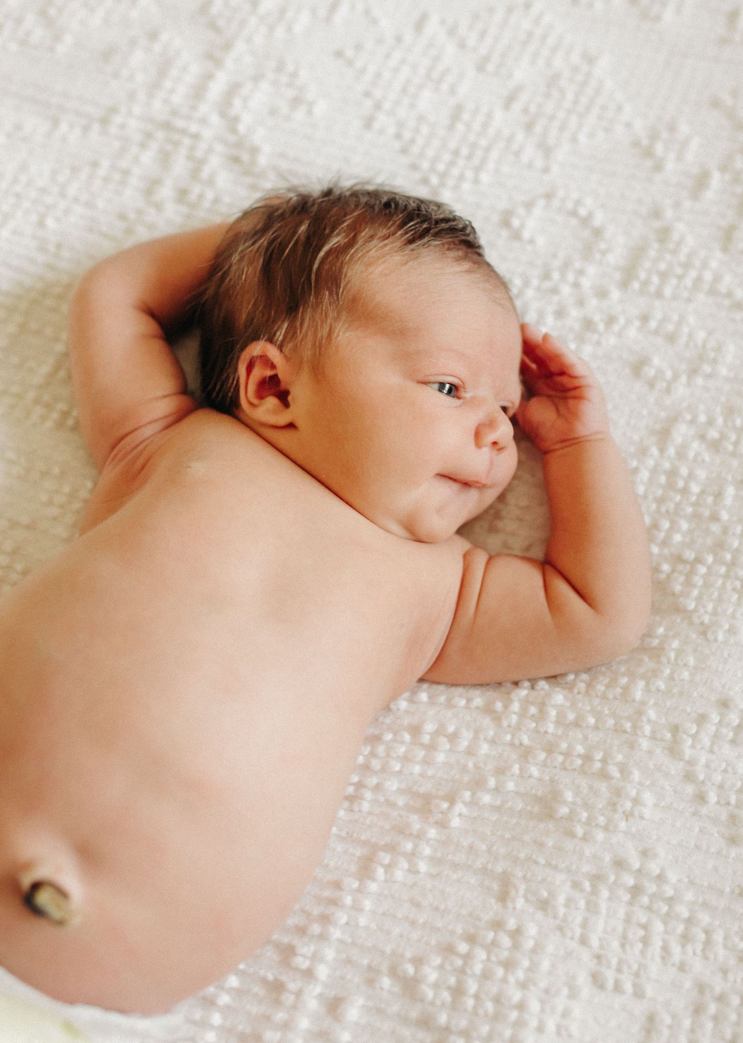 A newborn baby, laying on a visage blanket, stretches her arms.