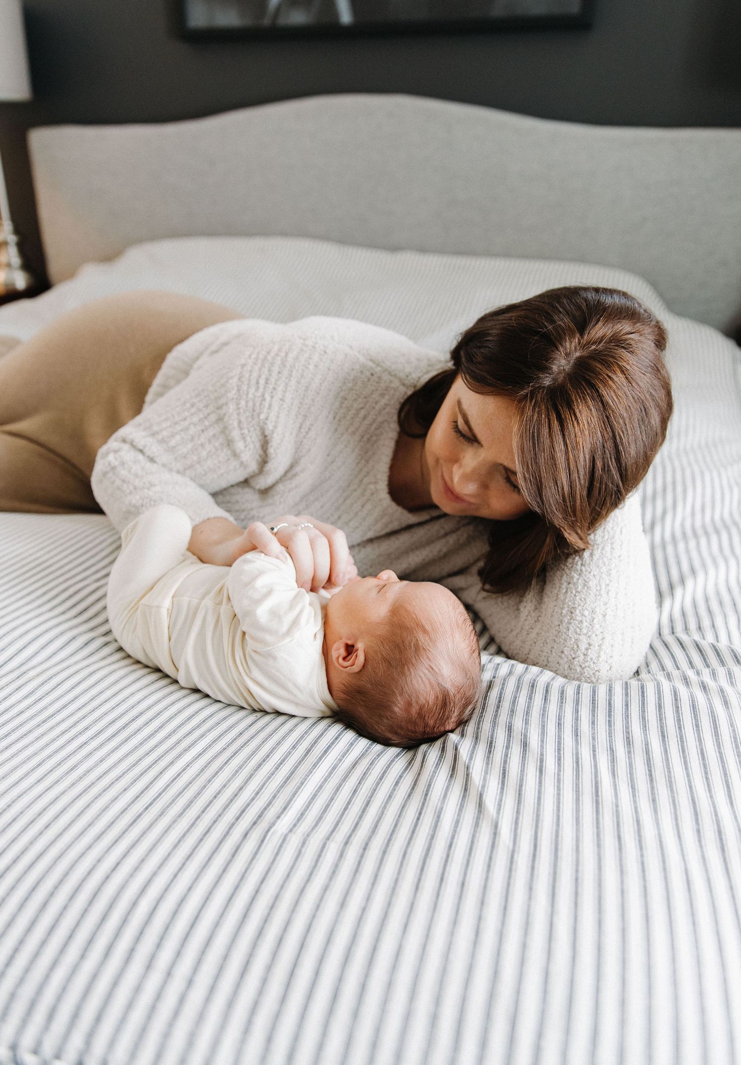 Tender moment between parent and baby on striped bedding in cozy bedroom.
