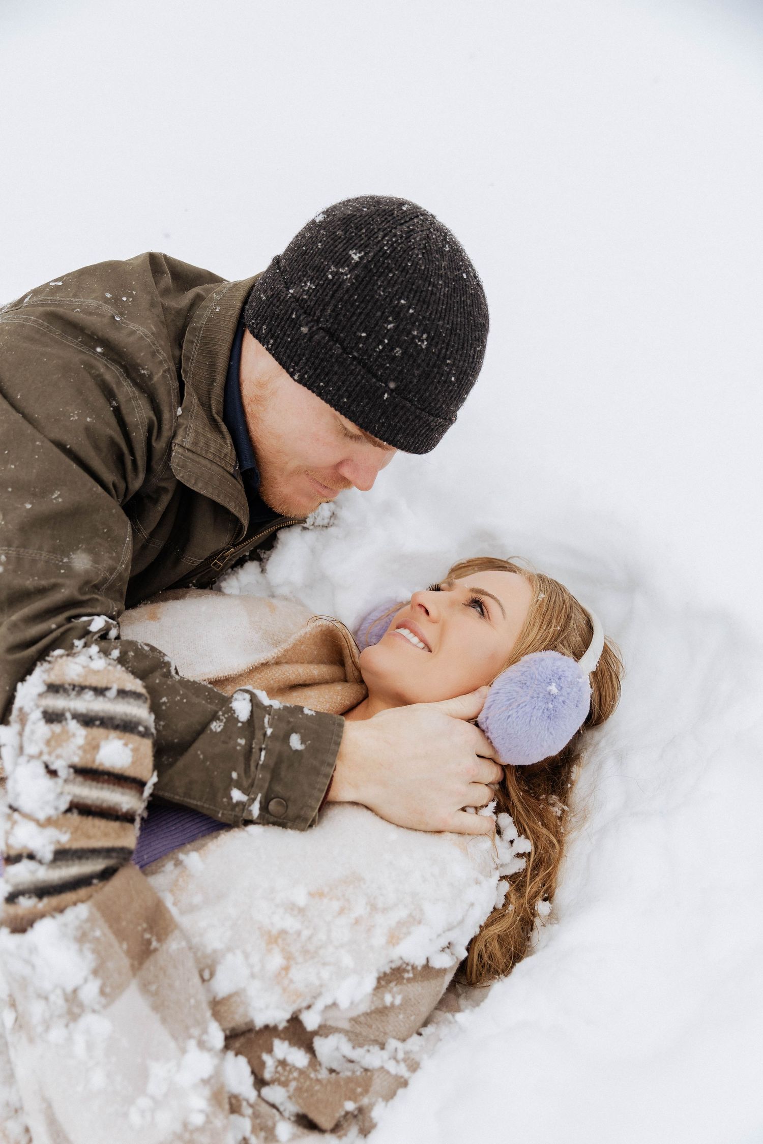 A couple shares a romantic moment lying in fresh snow during winter.