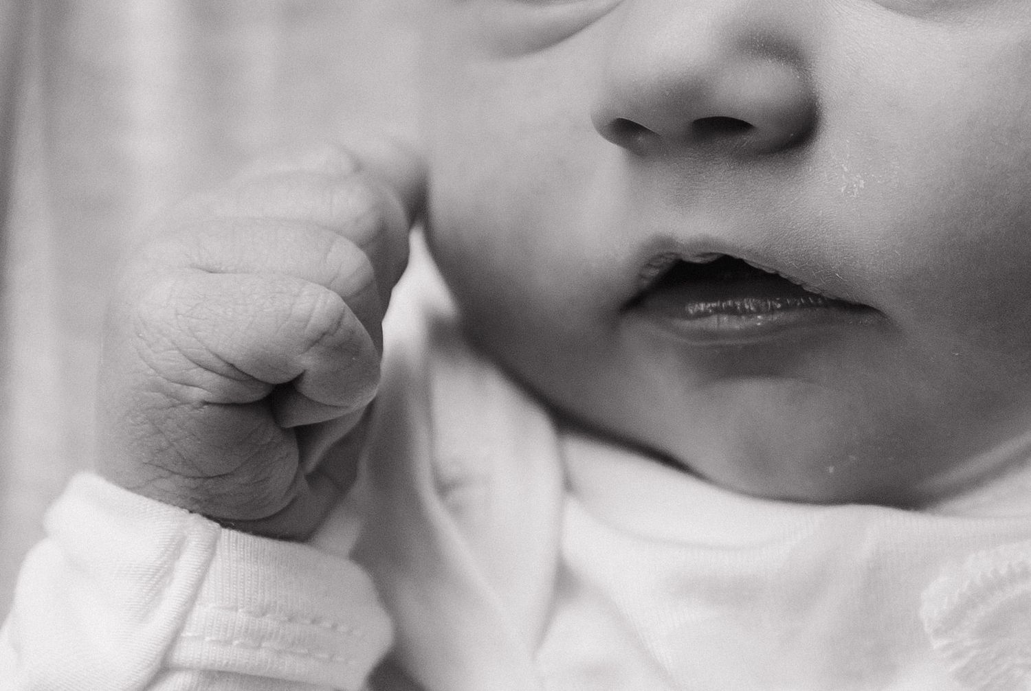 Black and white macro shot showing newborn's tiny fist and mouth details.