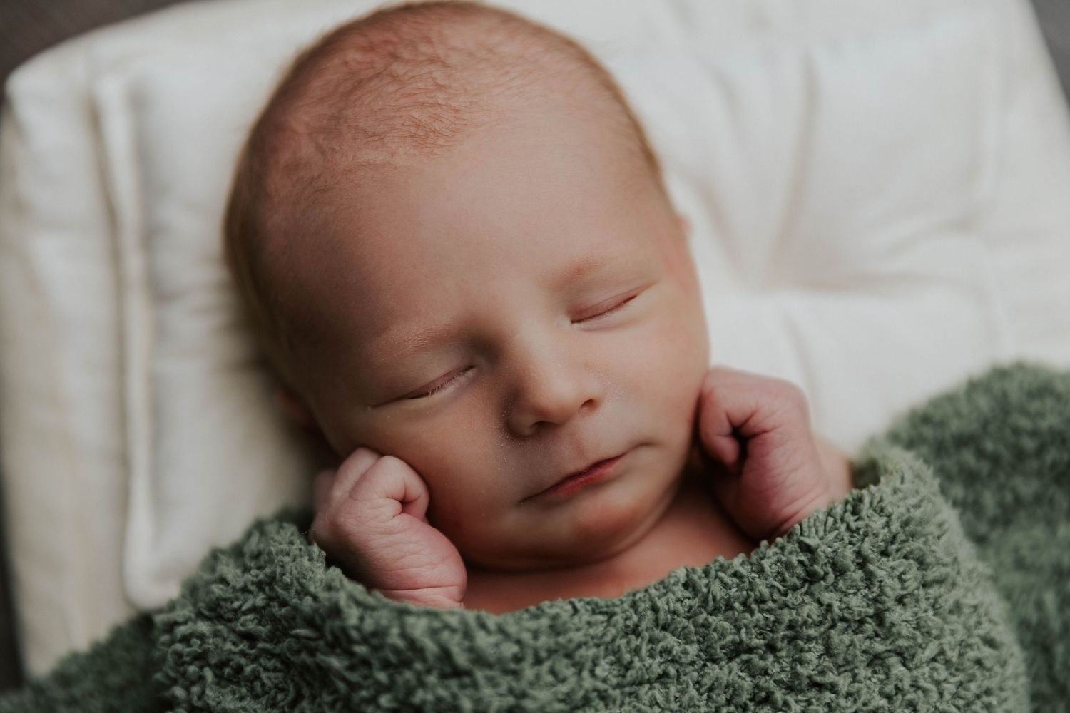 A newborn baby sleeping peacefully on a soft green blanket in black and white photography.