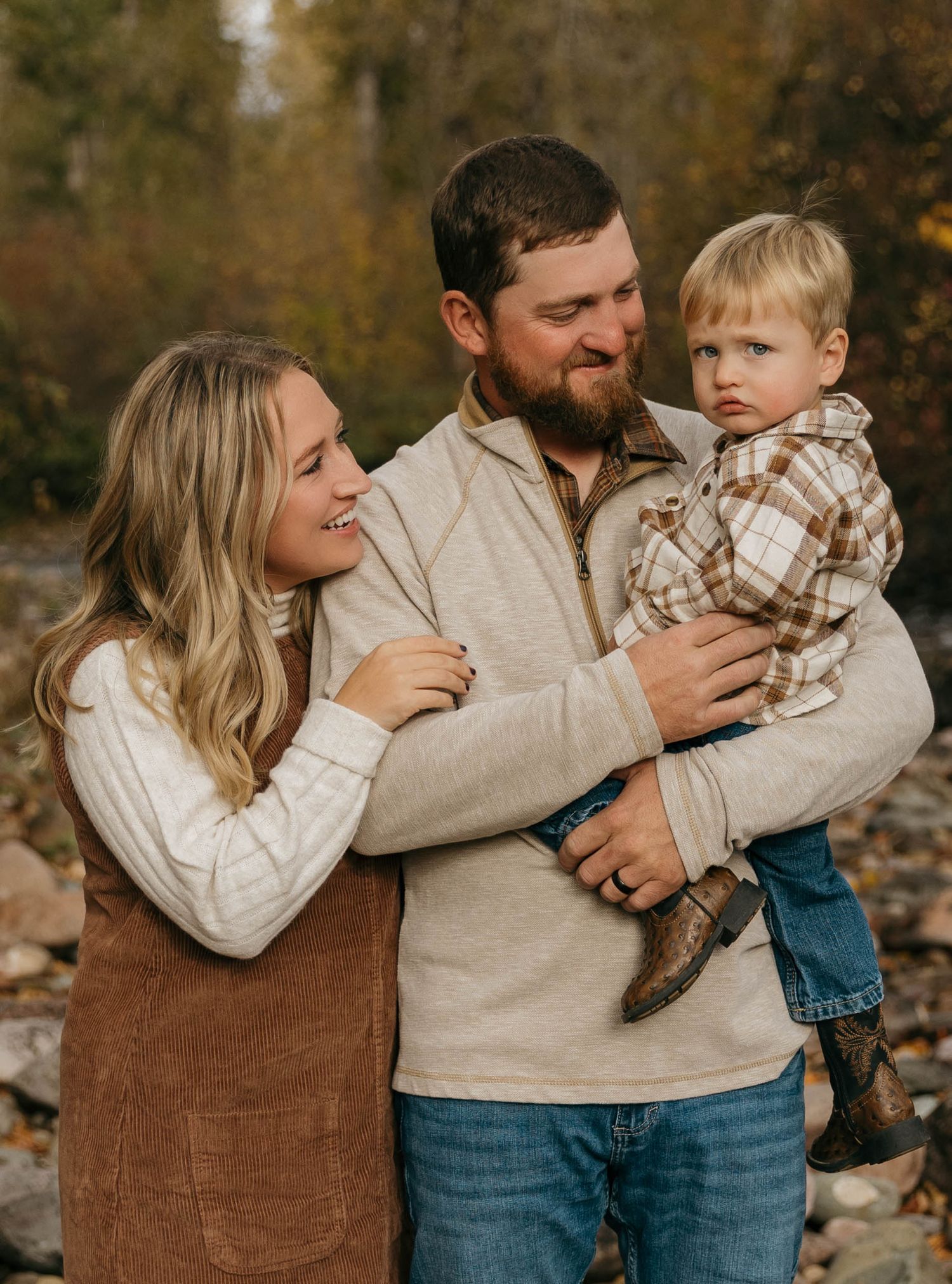 Family wearing coordinated cream and brown outfits share tender moments in an autumn outdoor setting.