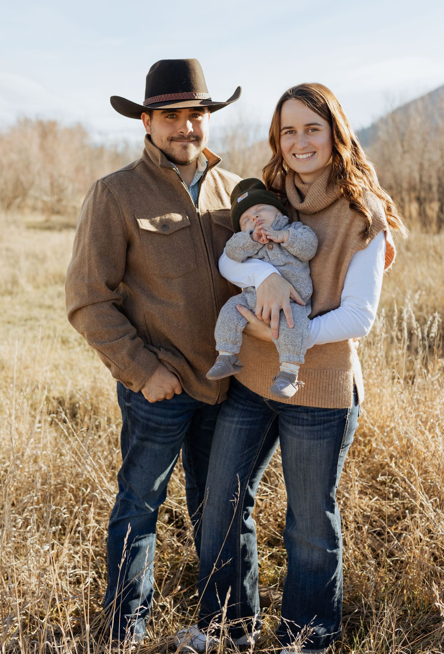 A family portrait in western attire standing in a rustic field setting.