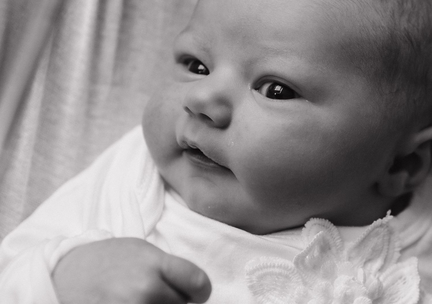 Black and white portrait of an alert newborn in white clothing.