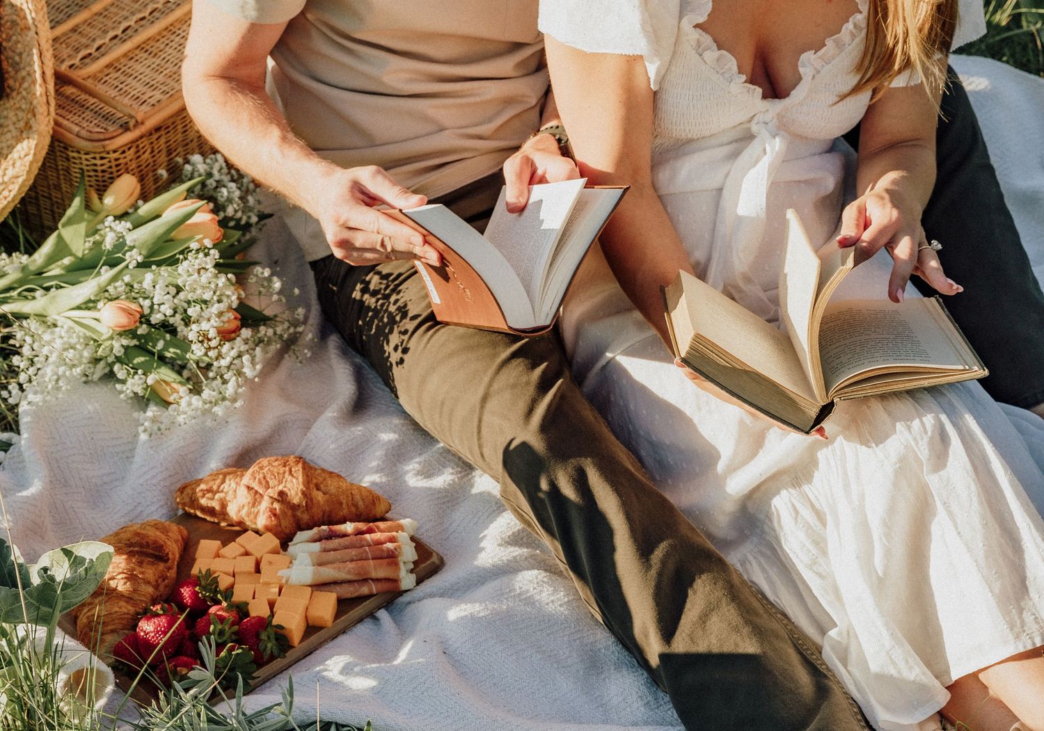 Overhead view of couple reading books during outdoor picnic with snacks.