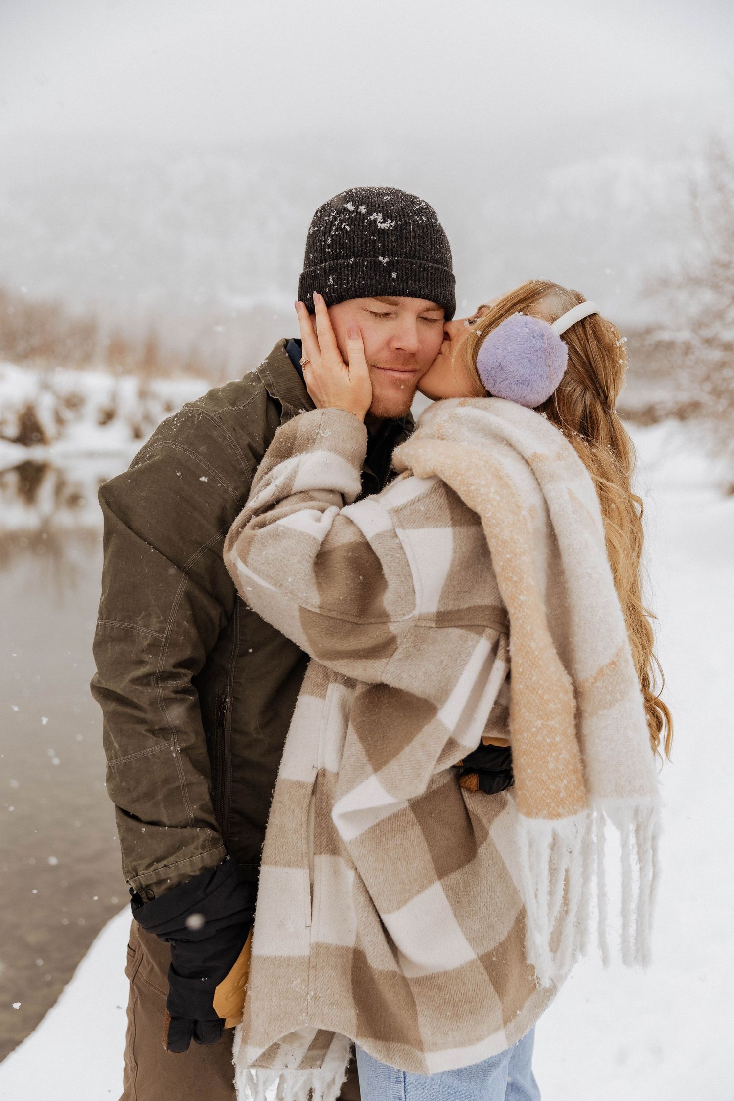 A tender winter moment between two people by a snowy lake.