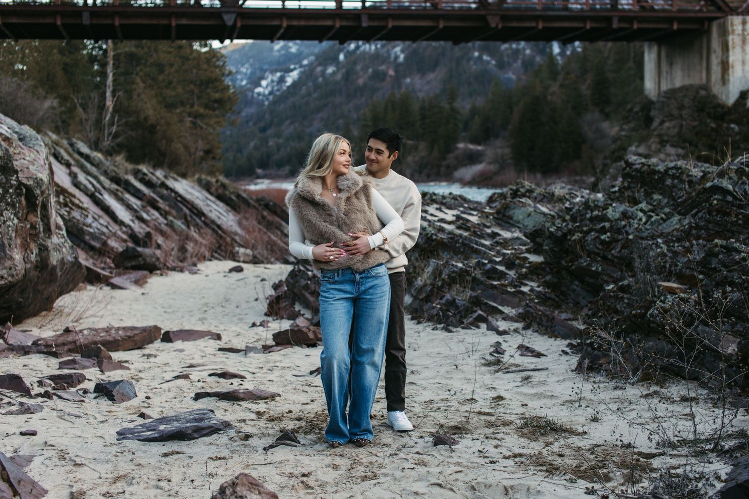 Couple holding hands while walking along a rocky beach during an overcast day.